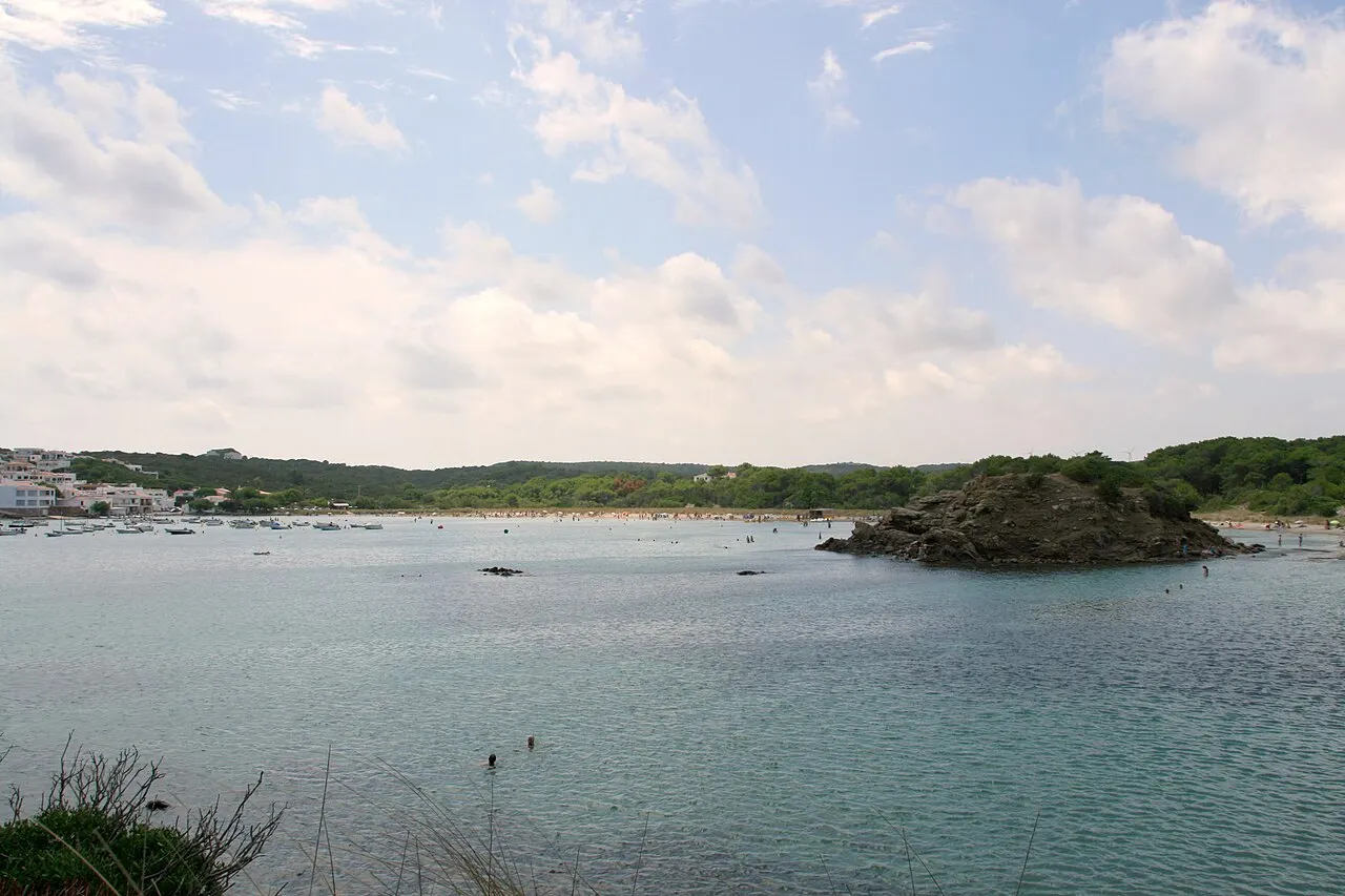 The bay of Es Grau, with calm water and a rocky islet, at the edge of the s'Albufera des Grau Natural Park.