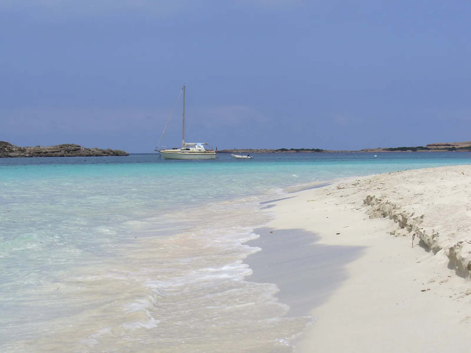 Velero fondeado frente a la playa de s'Alga, en s'Espalmador: agua turquesa, arena blanca y la isla al fondo.