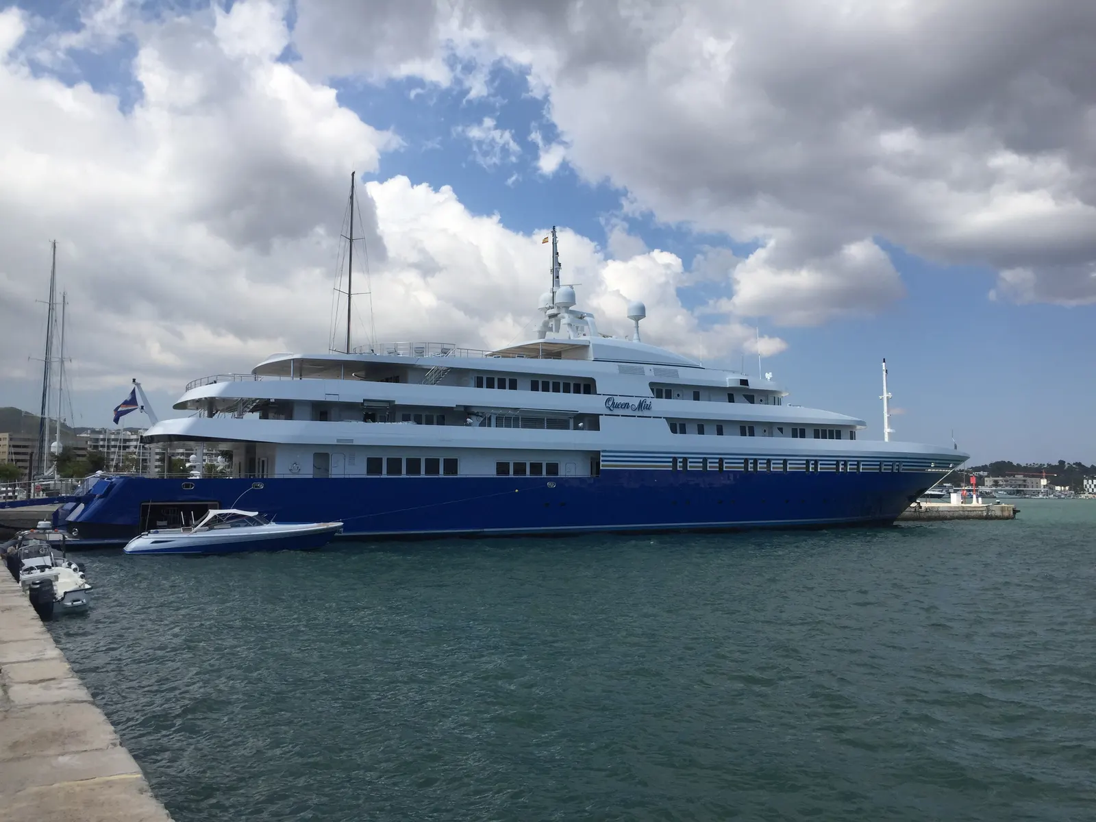 Un superyate blanco y azul amarrado en Marina Ibiza, con una lancha auxiliar al costado.