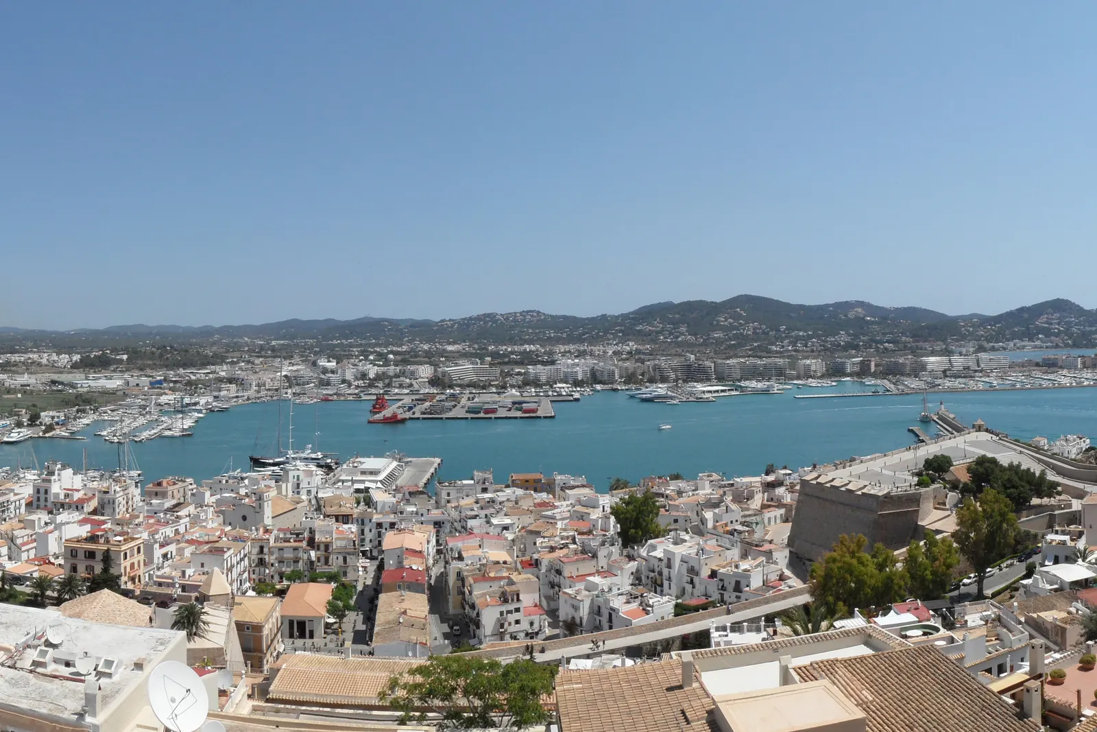 El puerto de Ibiza visto desde lo alto de la ciudad: tejados blancos en primer plano, la bahía con barcos amarrados y, al otro lado, la orilla de las marinas.