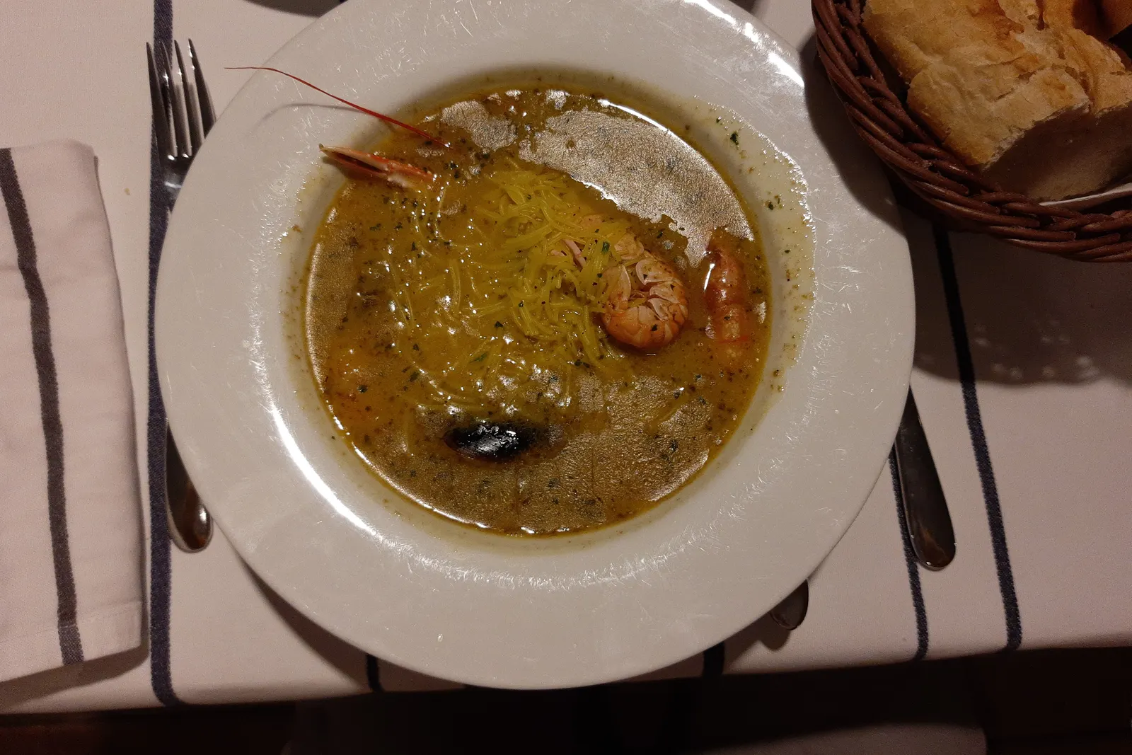 Un plato hondo de caldo de pescado con una gamba, servido con pan, en una mesa de Ibiza