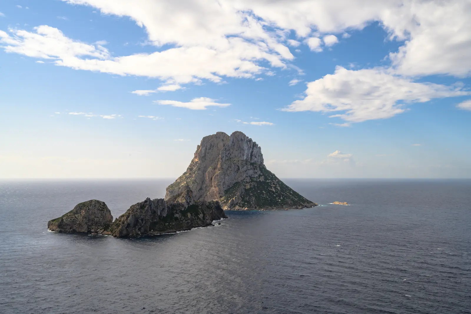 Es Vedrà y es Vedranell recortados sobre un mar en calma, vistos desde el aire con el cielo despejado.
