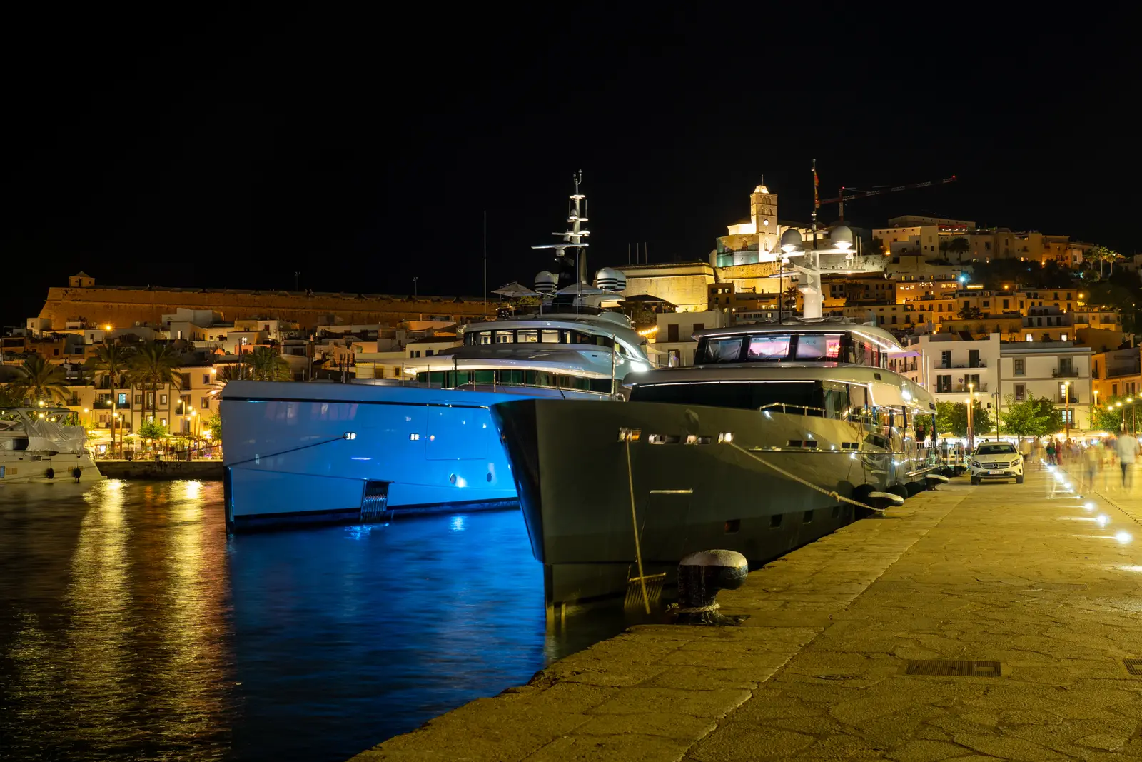 Grandes yates amarrados de noche en el puerto de Ibiza, con las luces de Dalt Vila iluminada al fondo.