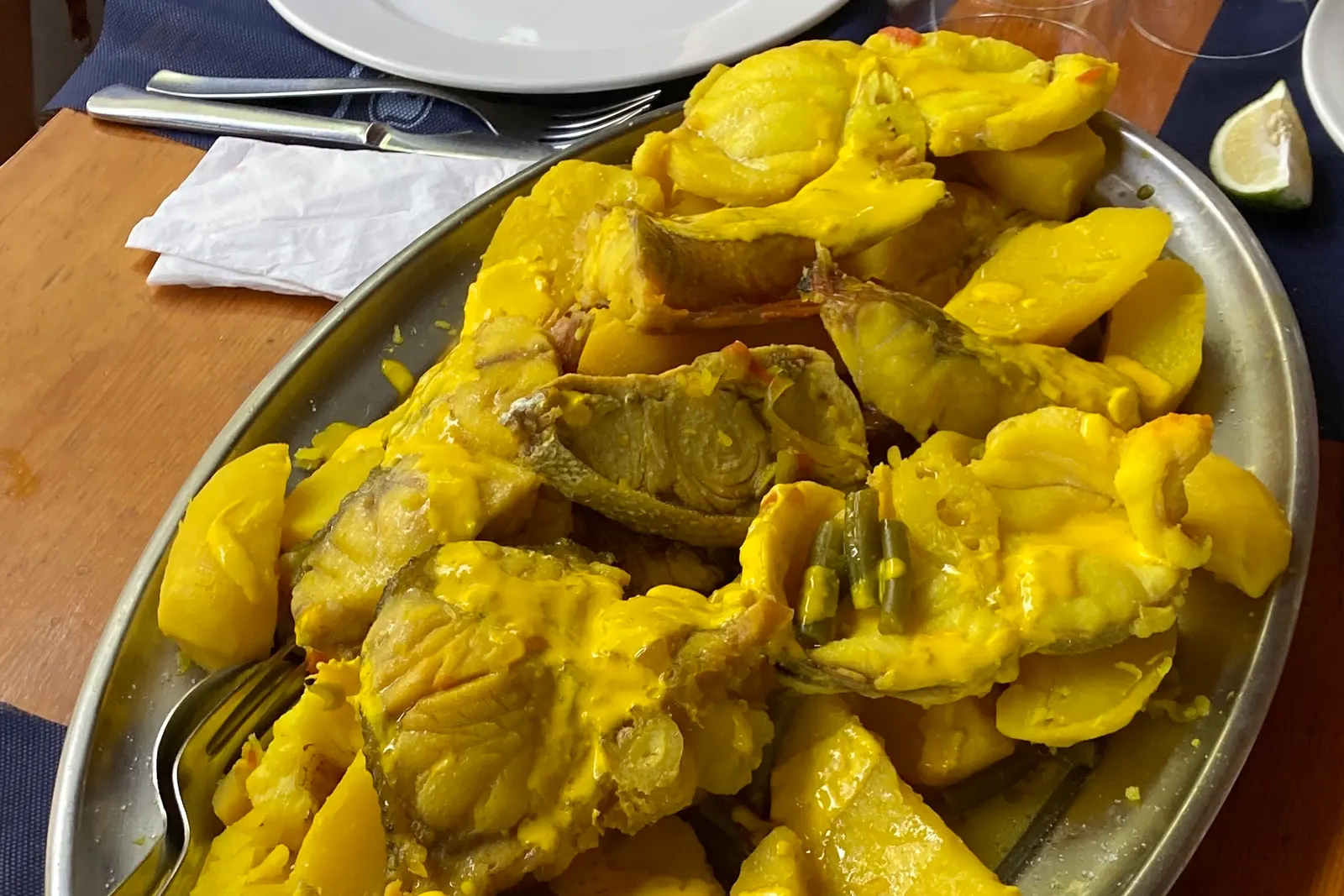 Bullit de peix: pescado y patatas en salsa amarilla de azafrán, servidos en una fuente metálica sobre la mesa de un restaurante.