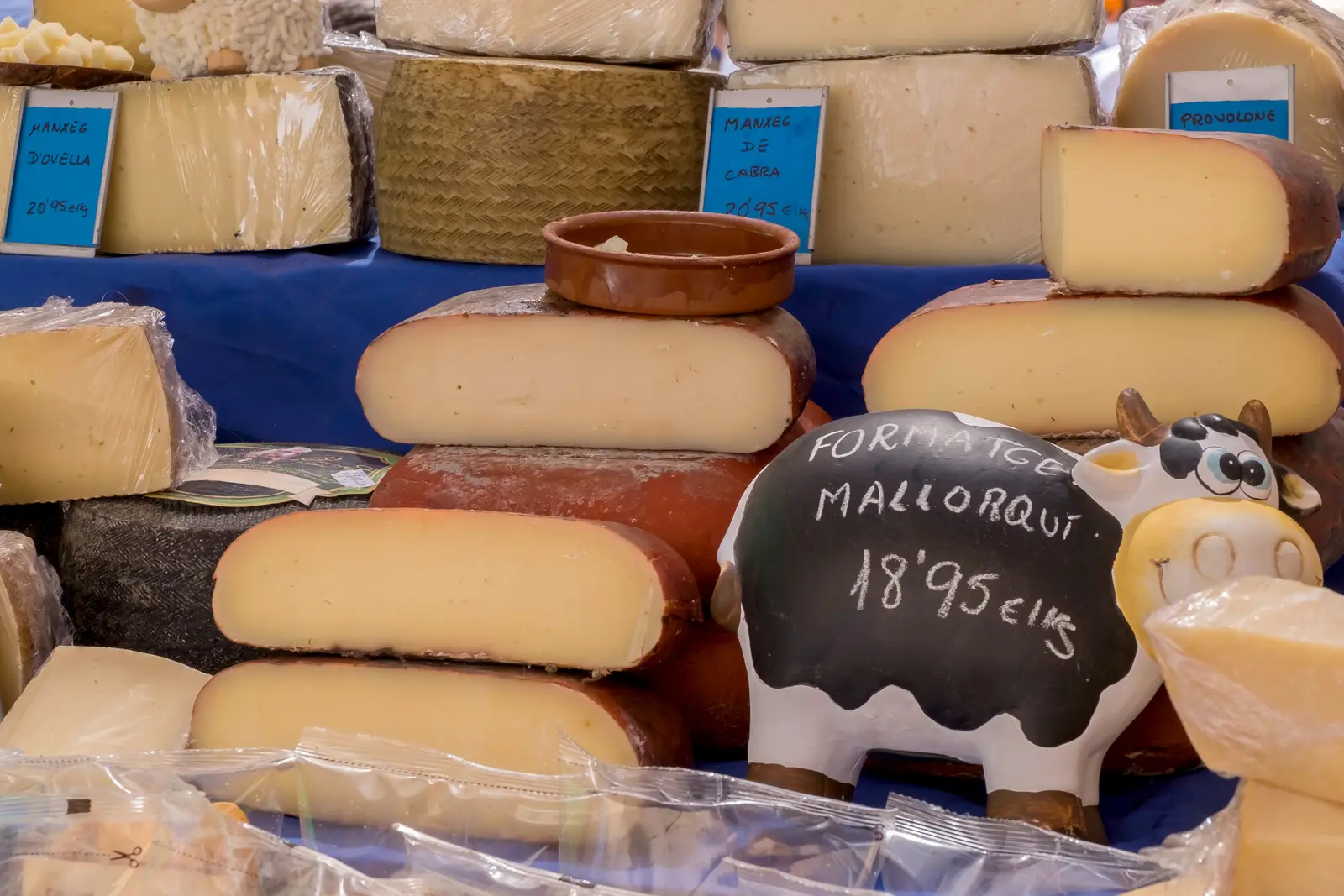 Puesto de quesos en un mercado de Mallorca, con una pizarra que anuncia formatge mallorquí y una vaca de cerámica.