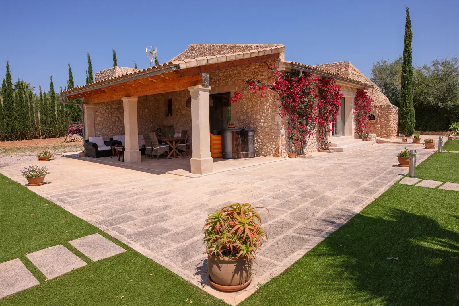 Finca mallorquina de piedra al anochecer, con porche de vigas de madera, buganvilla en la fachada y cipreses al fondo.