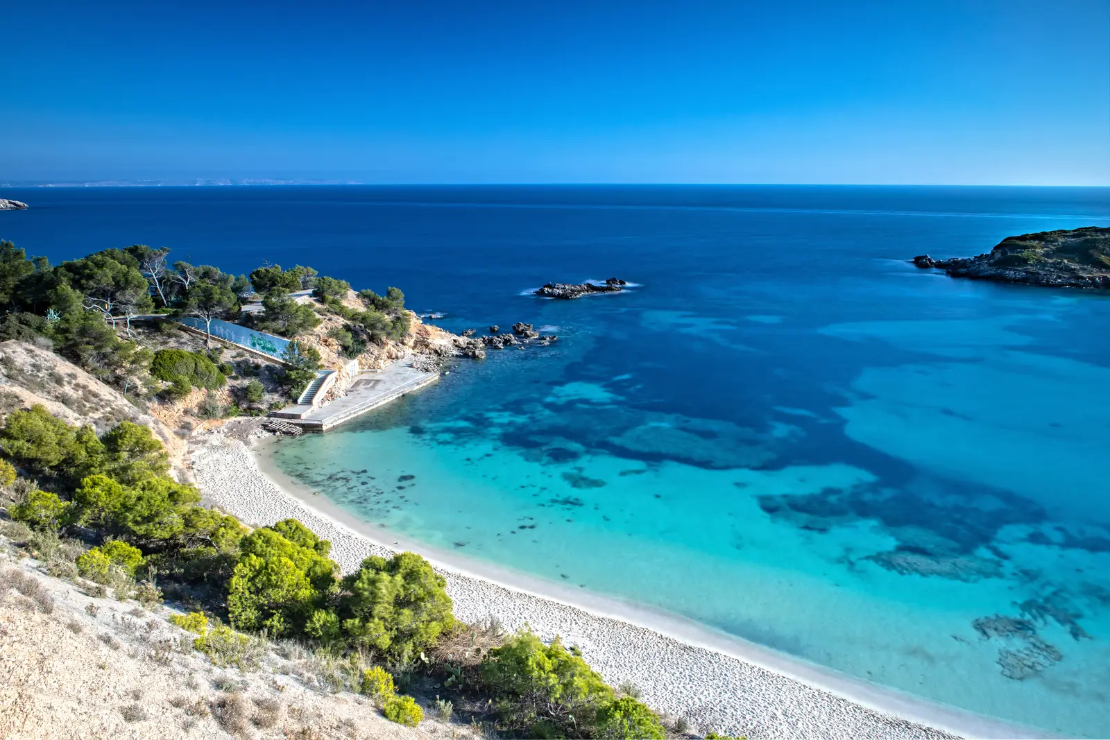 Cala de agua turquesa rodeada de pinos en la costa de Mallorca, vista desde lo alto del acantilado.