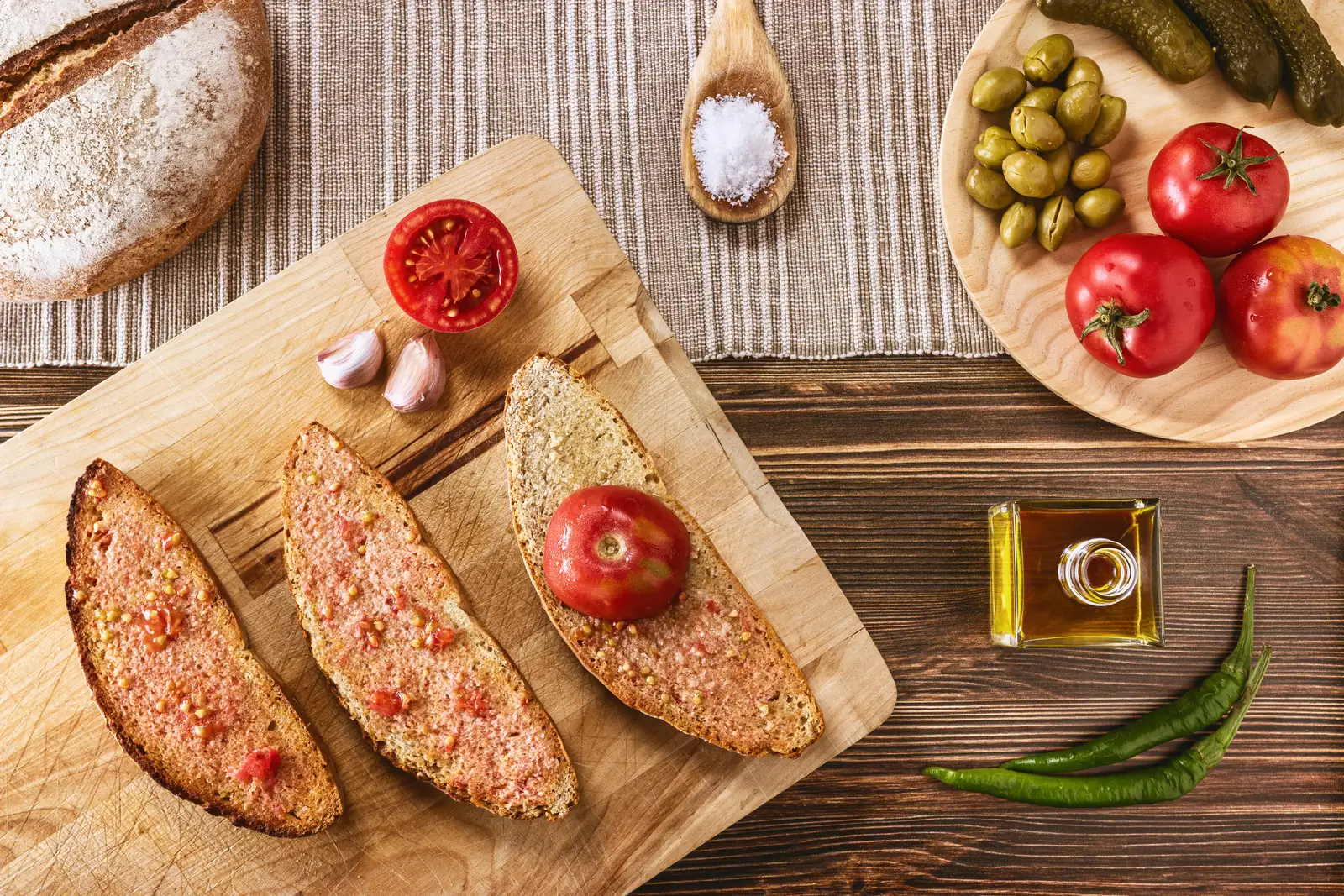 Pa amb oli mallorquín sobre tabla de madera, con tomate de ramallet, ajo, aceite de oliva y aceitunas.