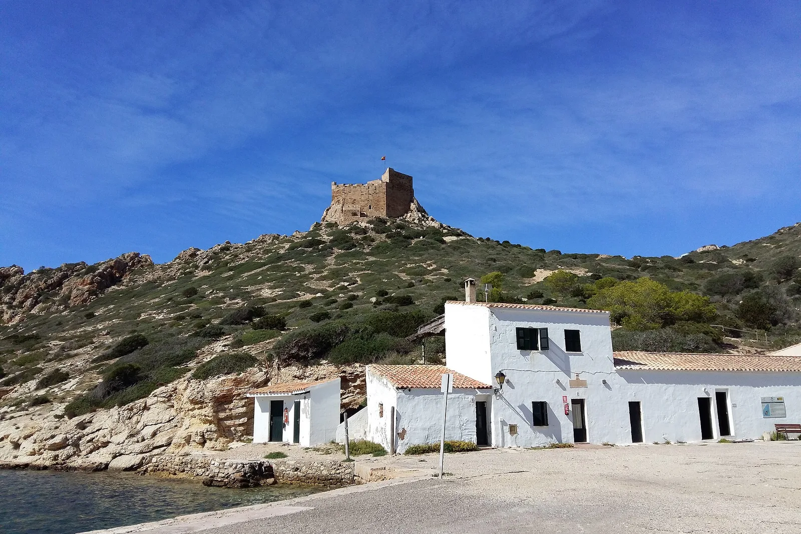 El castillo de Cabrera, en lo alto de la colina, sobre las casas blancas del puerto y el agua quieta de la cala.