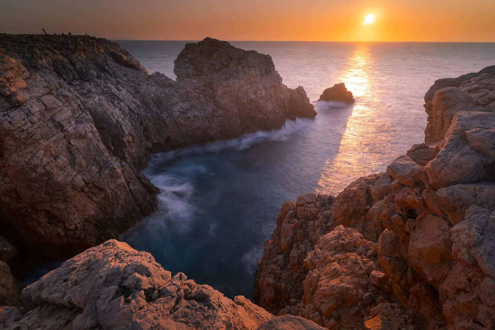 Atardecer dorado sobre el mar en calma y los acantilados de la costa oeste de Menorca, con el sol cayendo directamente sobre el agua.