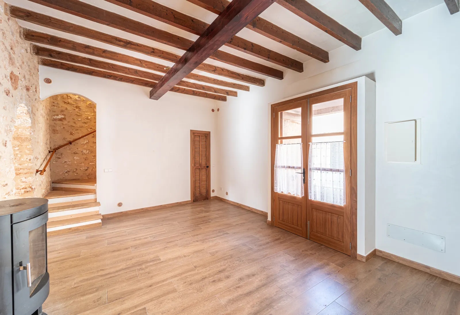 Interior de una casa mediterránea de piedra, con vigas de madera y escalera.