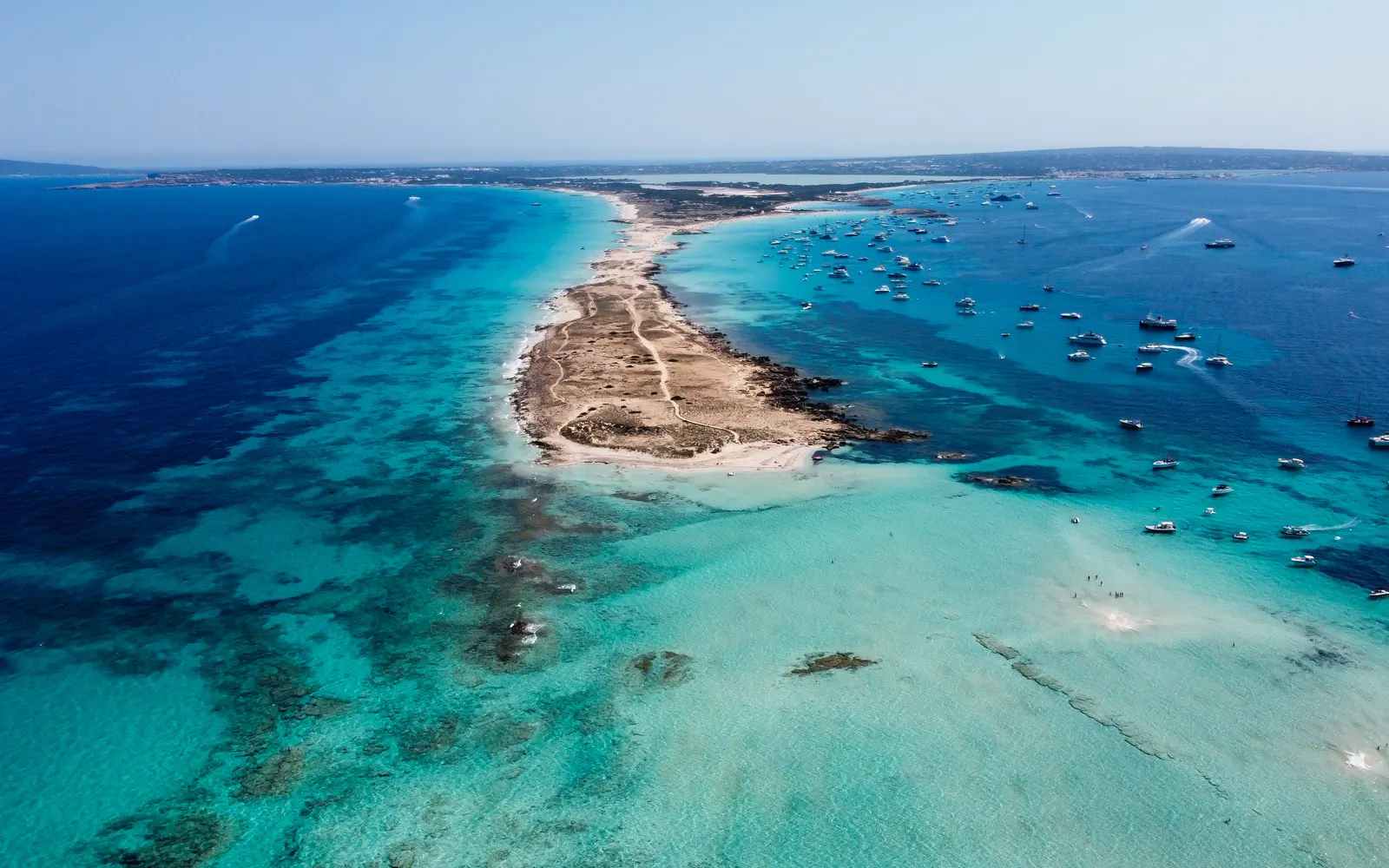 Vista aérea de la lengua de arena de ses Illetes, en Formentera, con veleros fondeados en agua turquesa a ambos lados.