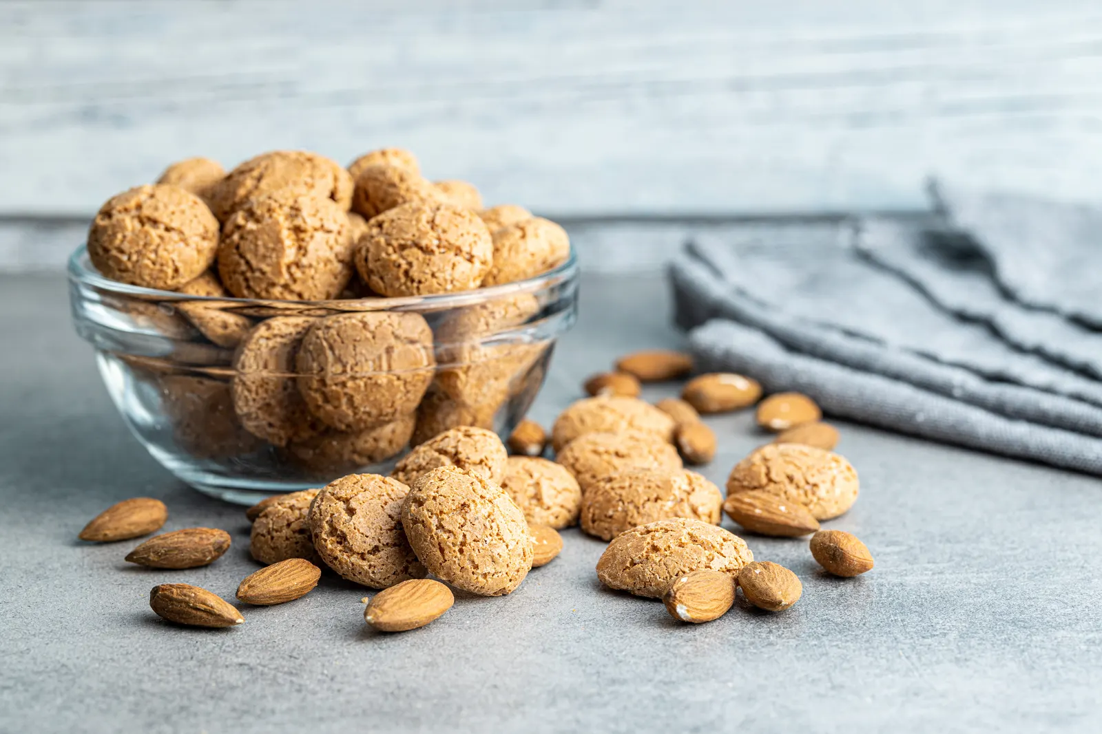 Galletas de almendra tipo amargos en un cuenco blanco, rodeadas de almendras enteras.