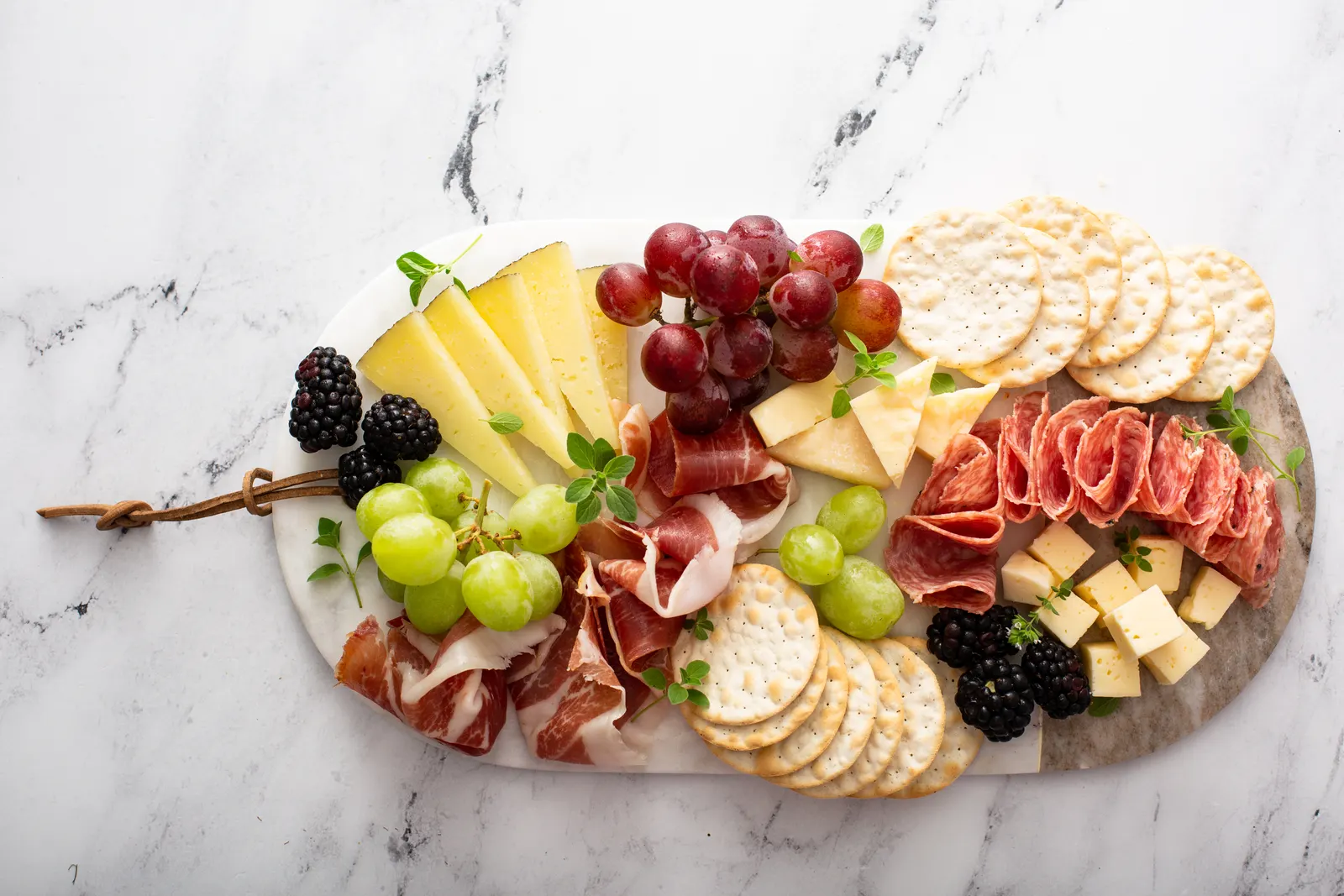 Tabla de madera con embutidos curados en lonchas, queso y un racimo de uvas, bien presentada.