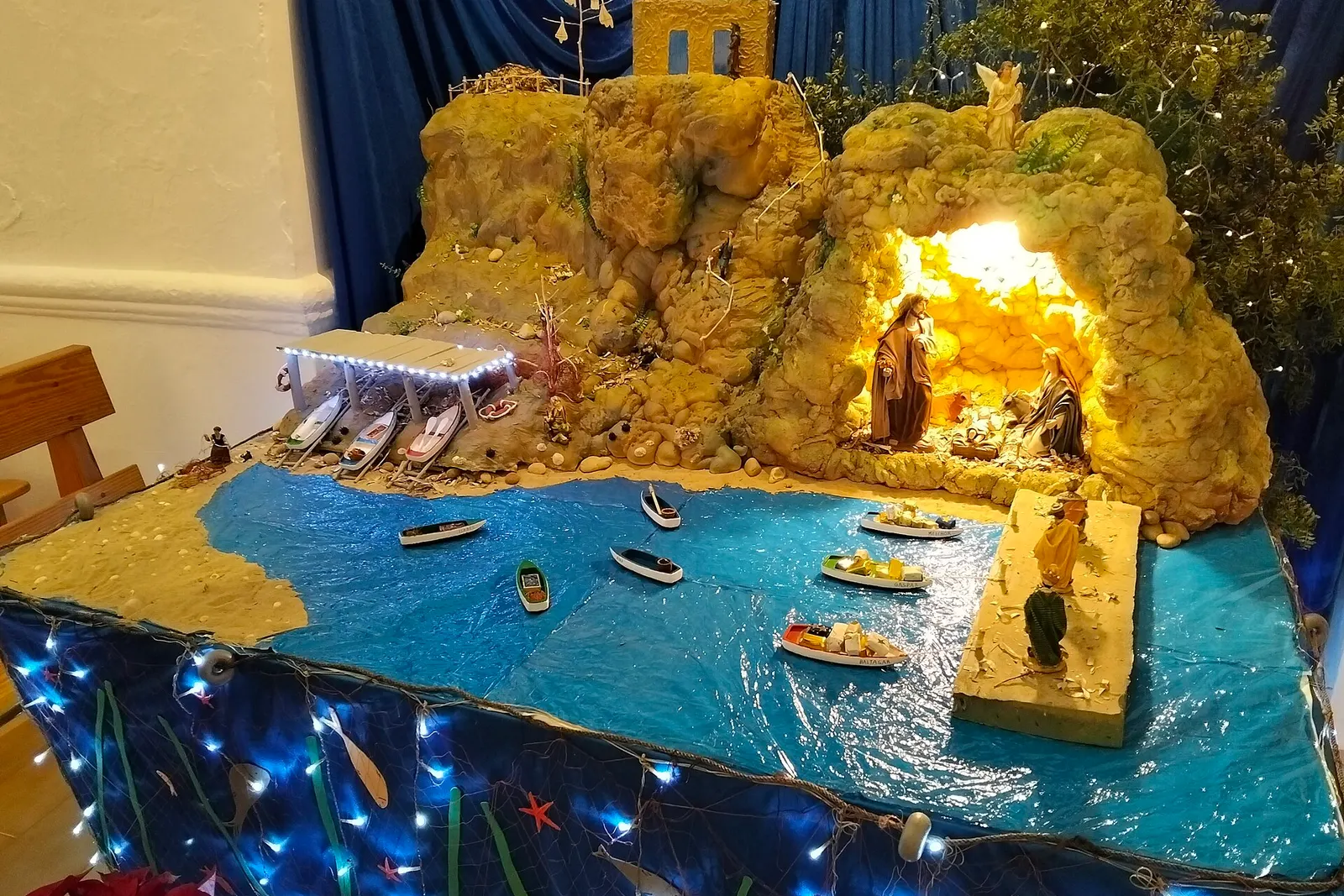 El belén de la iglesia de Sant Francesc Xavier, con barcas de pesca sobre un mar azul y el portal iluminado