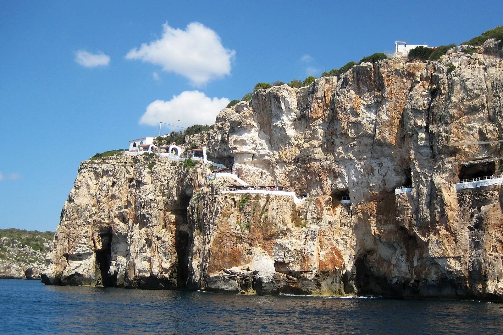 La scogliera di Cala en Porter vista dal mare, con le aperture della Cova d'en Xoroi nella parete di roccia