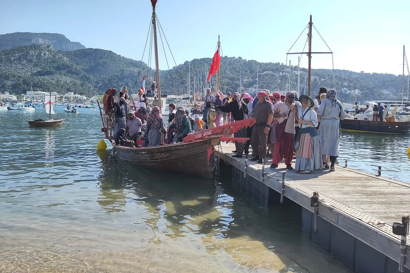 El desembarco de los moros en el Port de Sóller durante el Firó, con una barca de vela latina y el público en el muelle