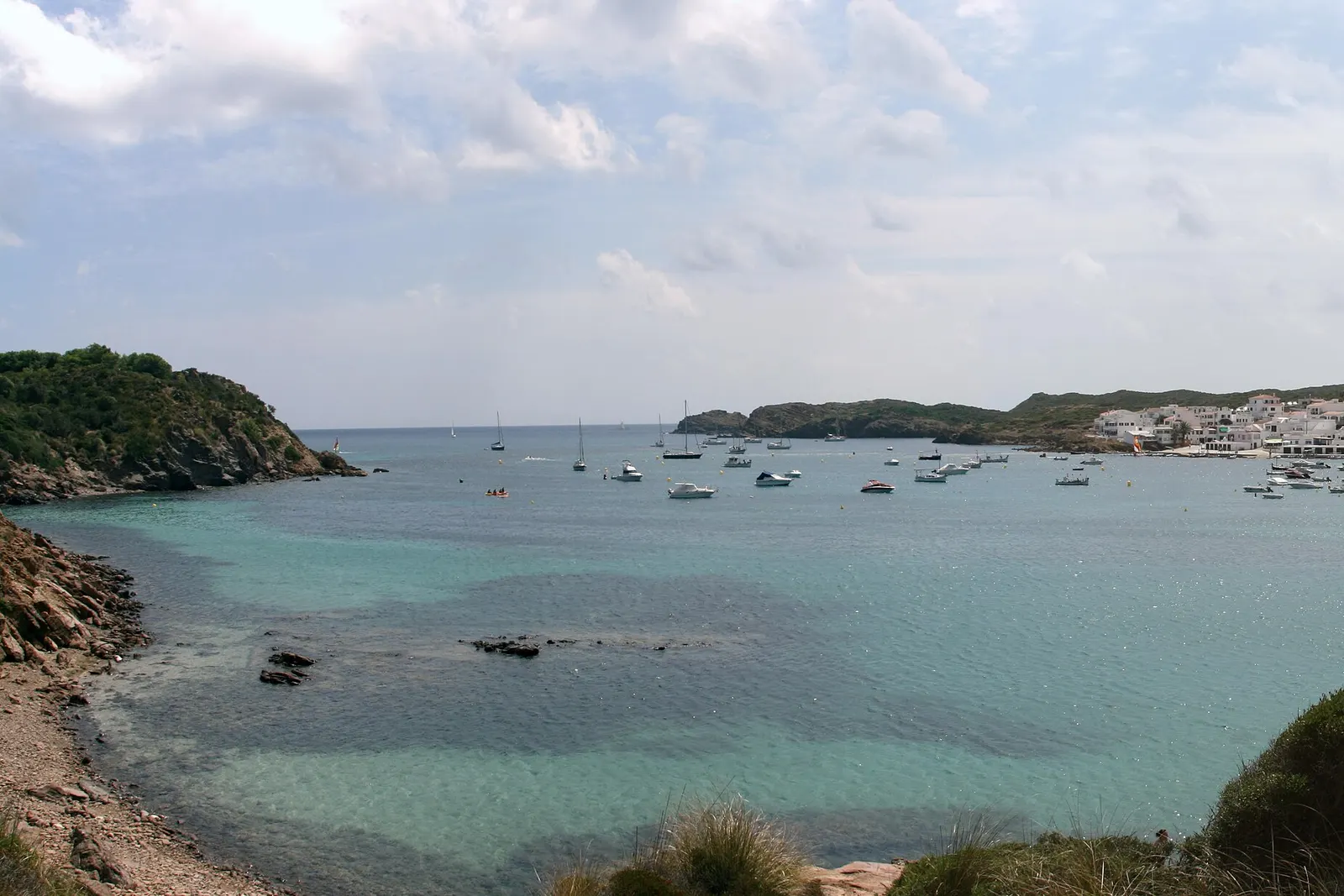 La baia di Es Grau, con il paese bianco sull'altra sponda e barche all'ancora