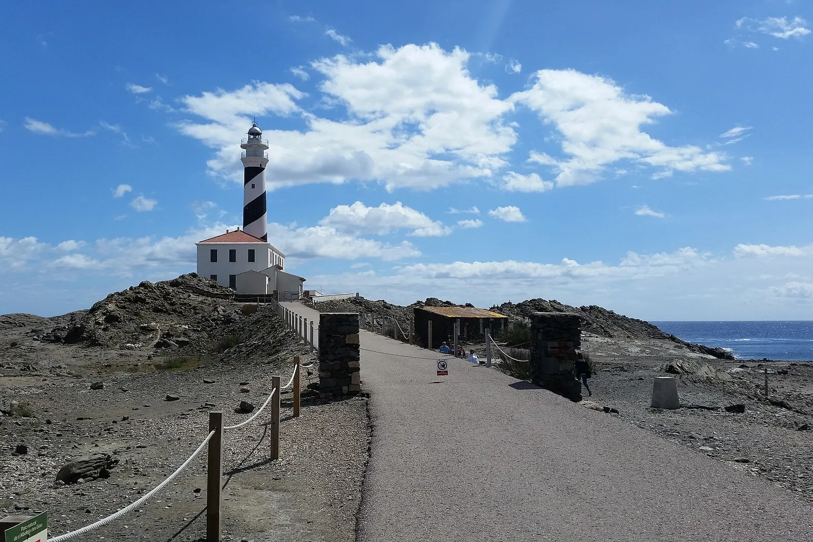 Il faro di Favàritx, bianco e nero, sul capo di ardesia scura, con la strada che vi arriva