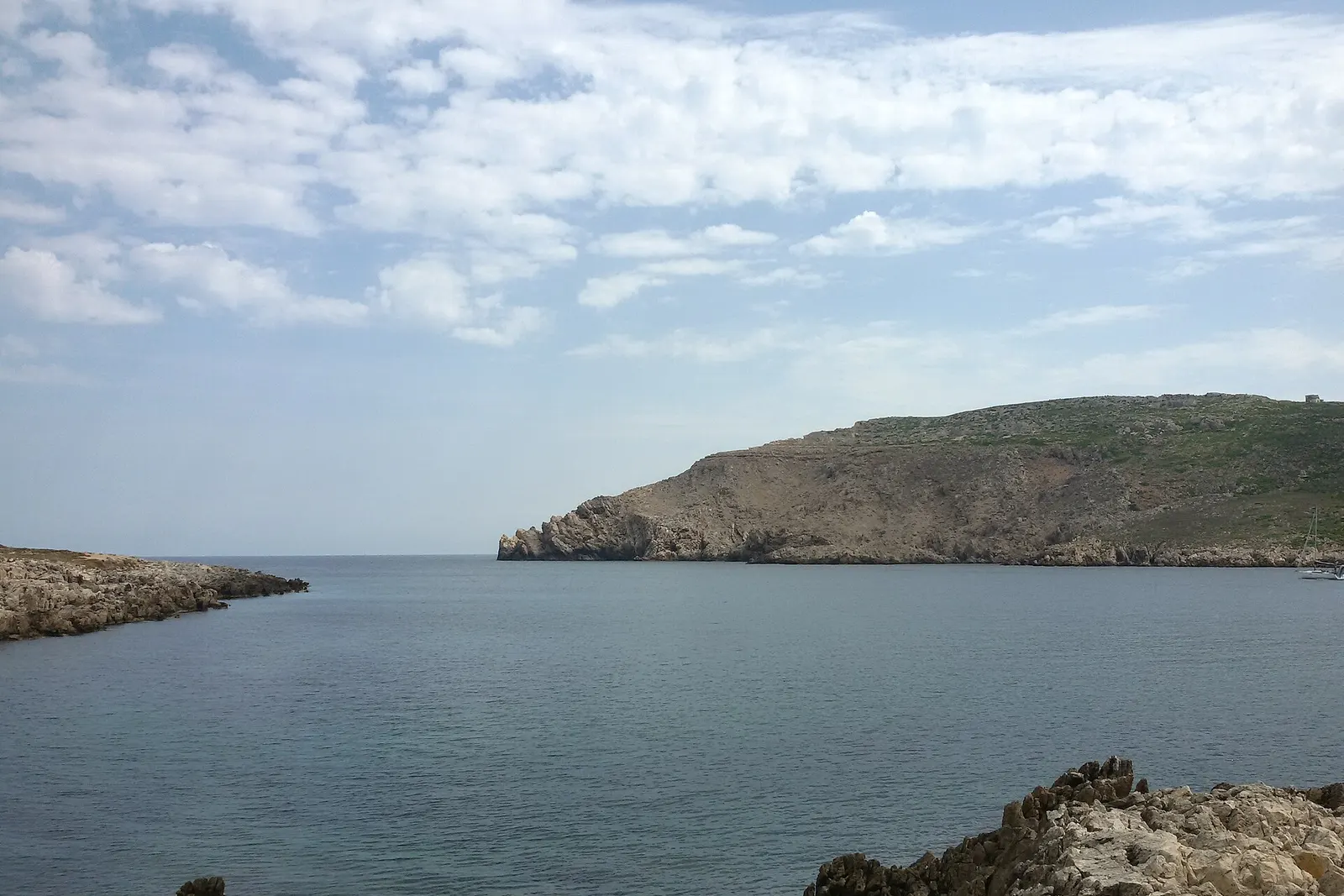 L'imboccatura della baia di Fornells, con la costa rocciosa in primo piano e il promontorio della Mola de Fornells a destra