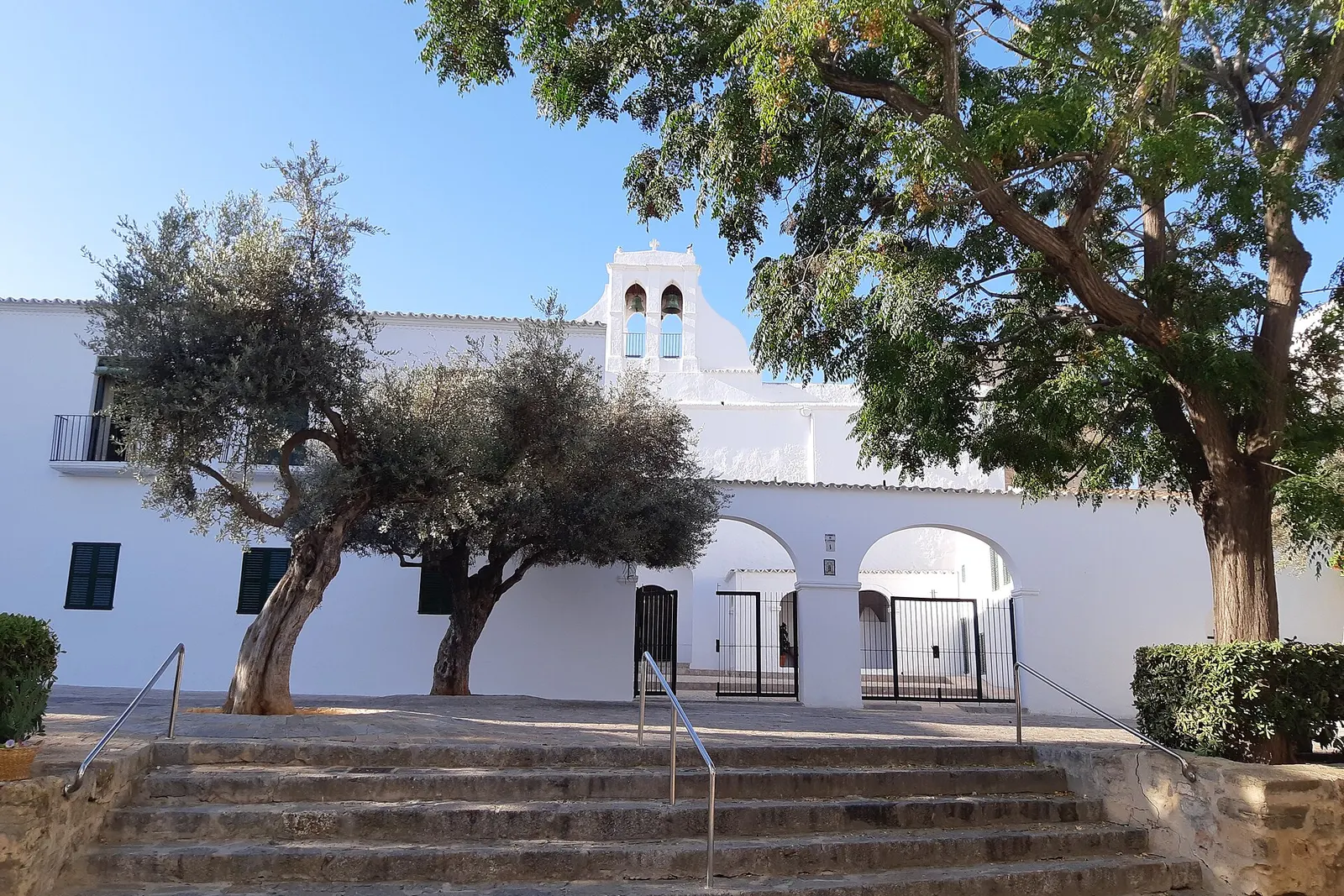 La iglesia blanca de Sant Antoni de Portmany, con su escalinata y los olivos de la plaza