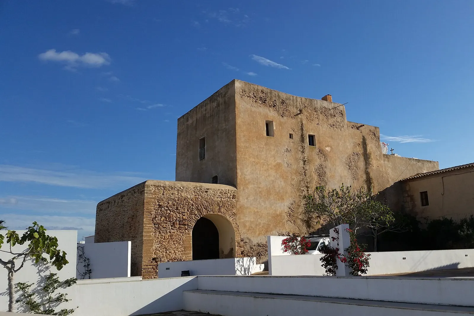 La iglesia fortificada de Sant Francesc Xavier vista desde atrás, con sus muros de piedra bajo el cielo azul