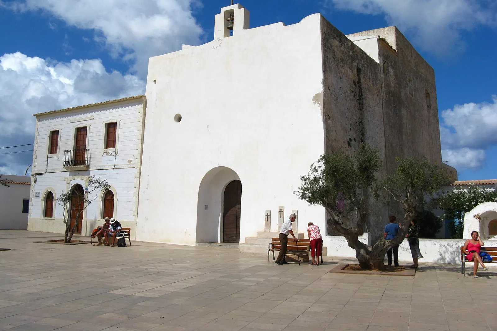 La iglesia fortificada de Sant Francesc Xavier, encalada, con la plaza y un olivo delante
