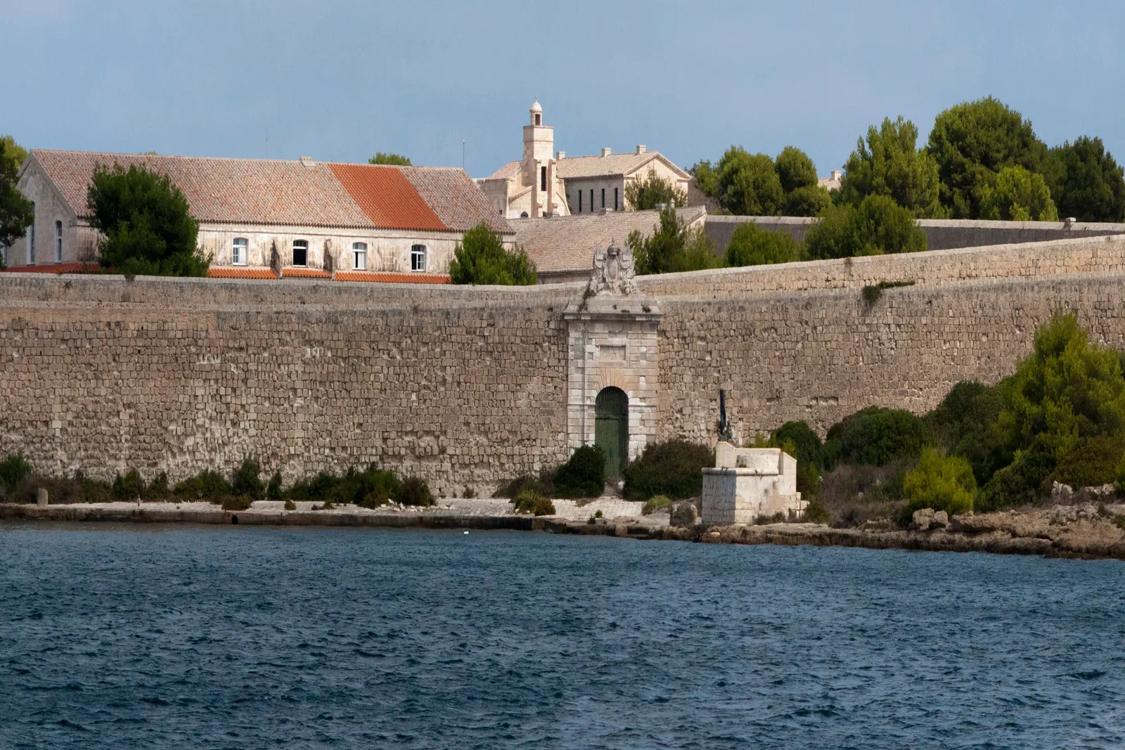 Le mura del Llatzeret sopra le acque del porto di Maó, con una torre sullo sfondo