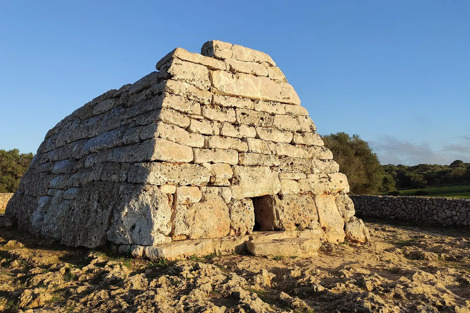 La Naveta des Tudons, un sepolcro preistorico in pietra a forma di scafo capovolto, con luce del tardo pomeriggio