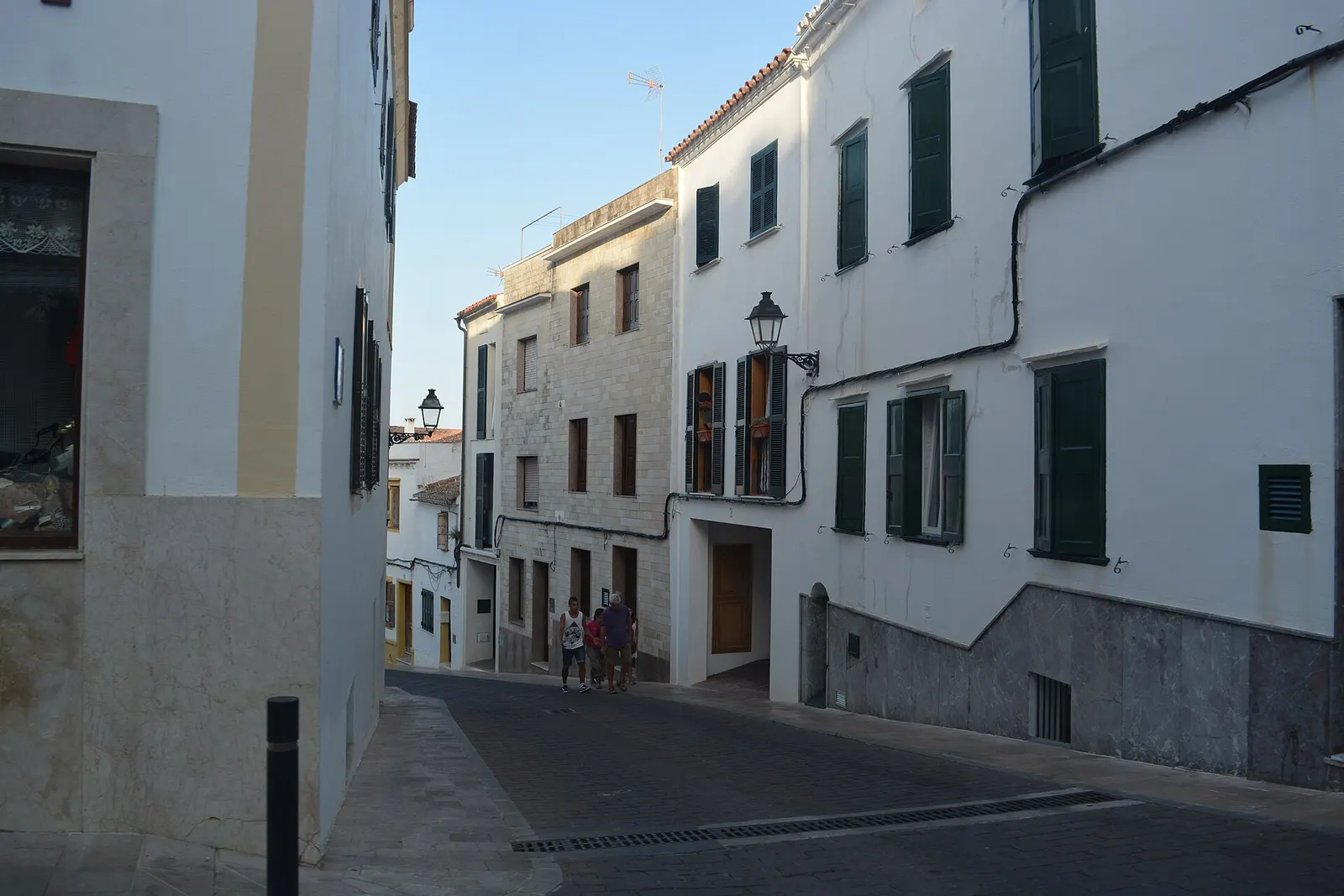 Calle empedrada de Alaior entre casas blancas con persianas verdes