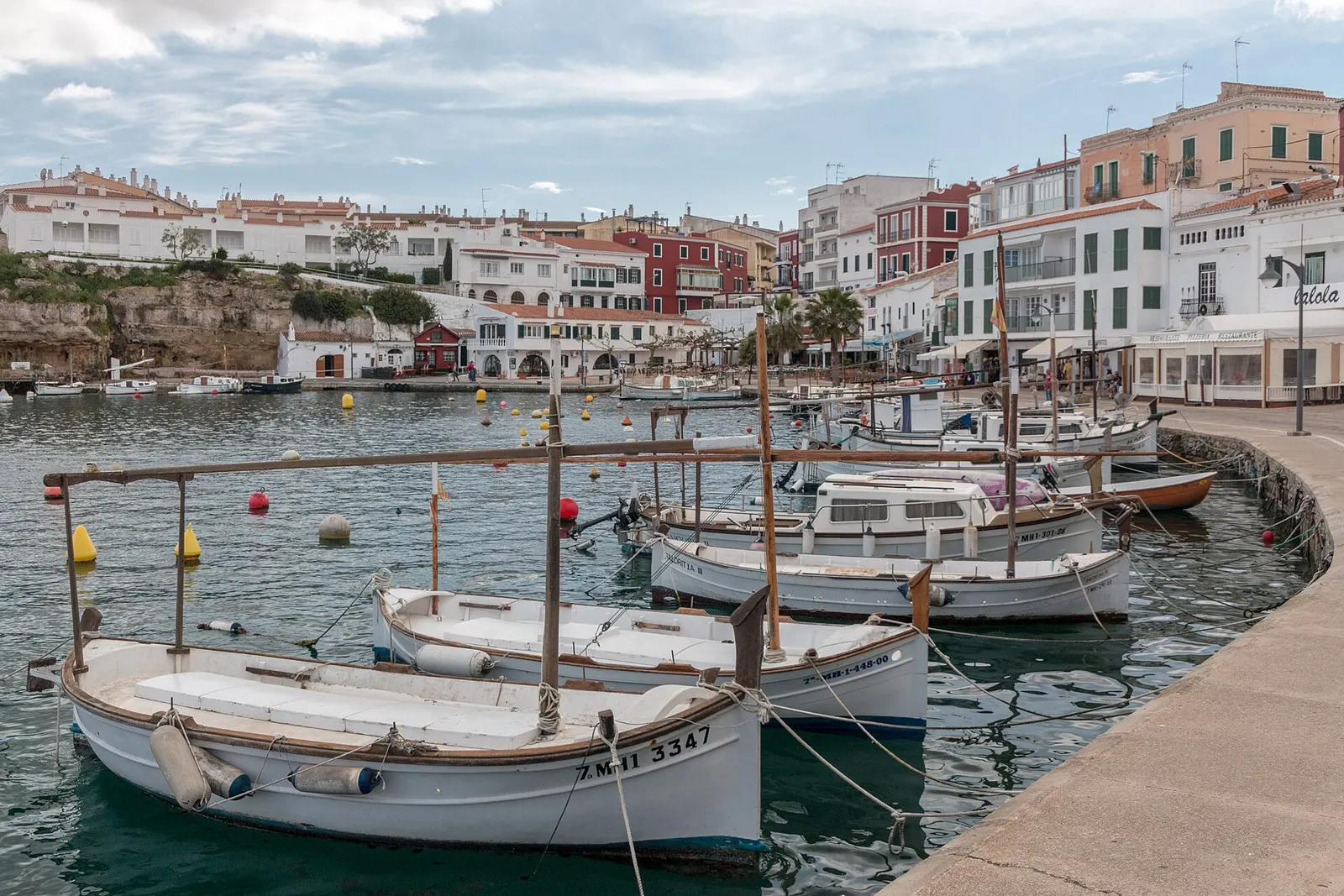 Llaüts de madera amarrados en fila en el puerto, frente a las casas de Es Castell