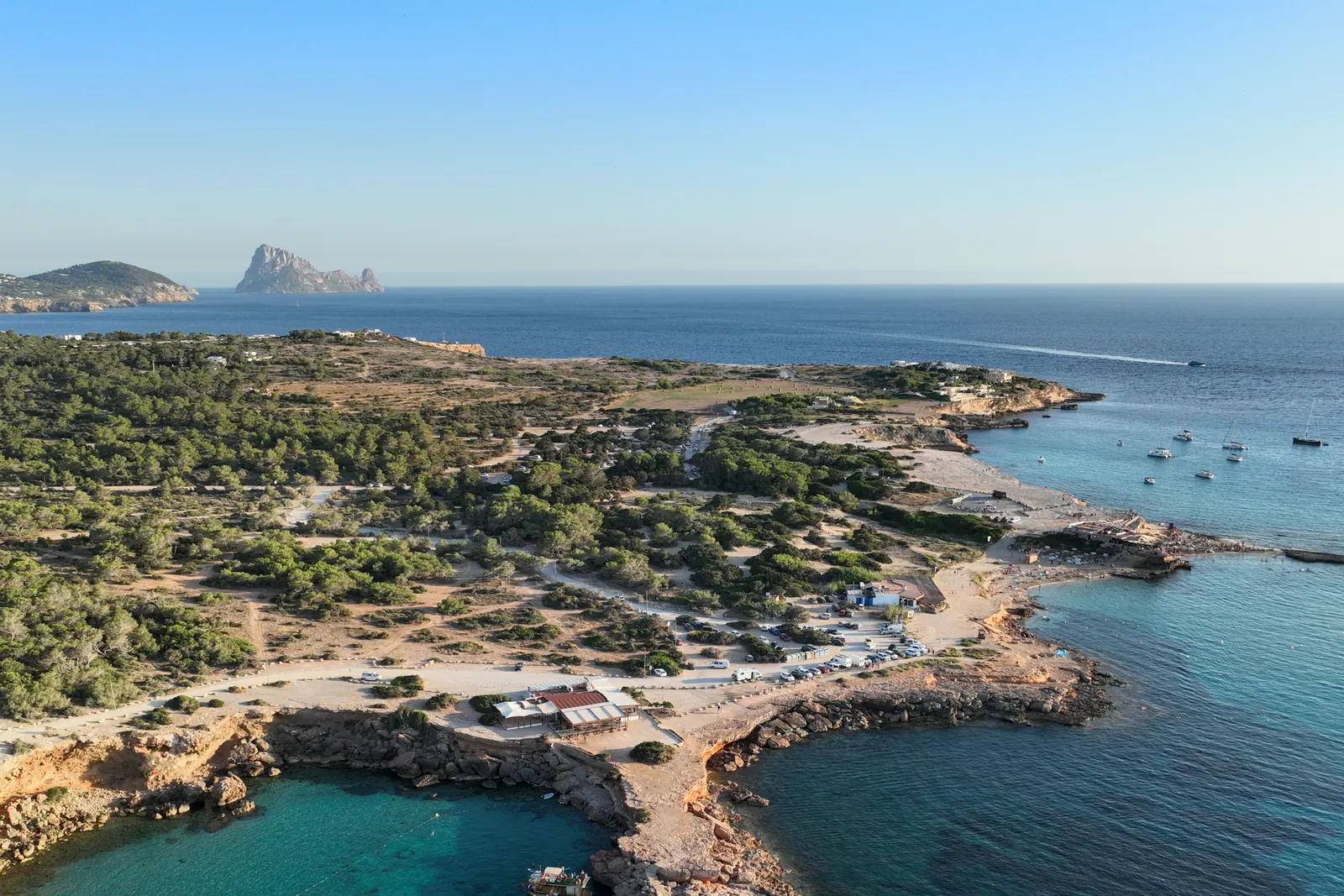 Vista aérea de Cala Comte, con el agua turquesa sobre fondo claro y varios veleros fondeados