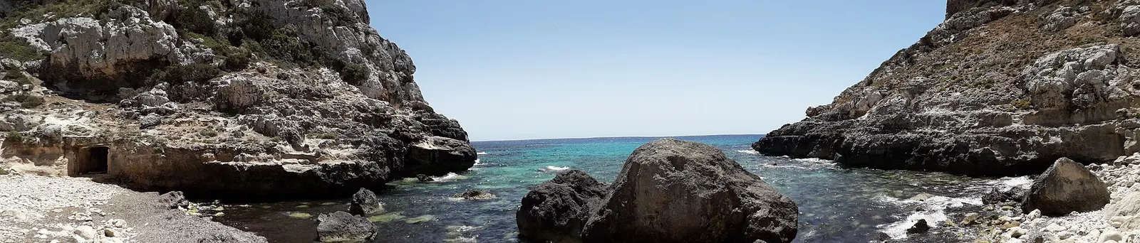 El agua turquesa de Cala Llucalari entre grandes bloques de roca