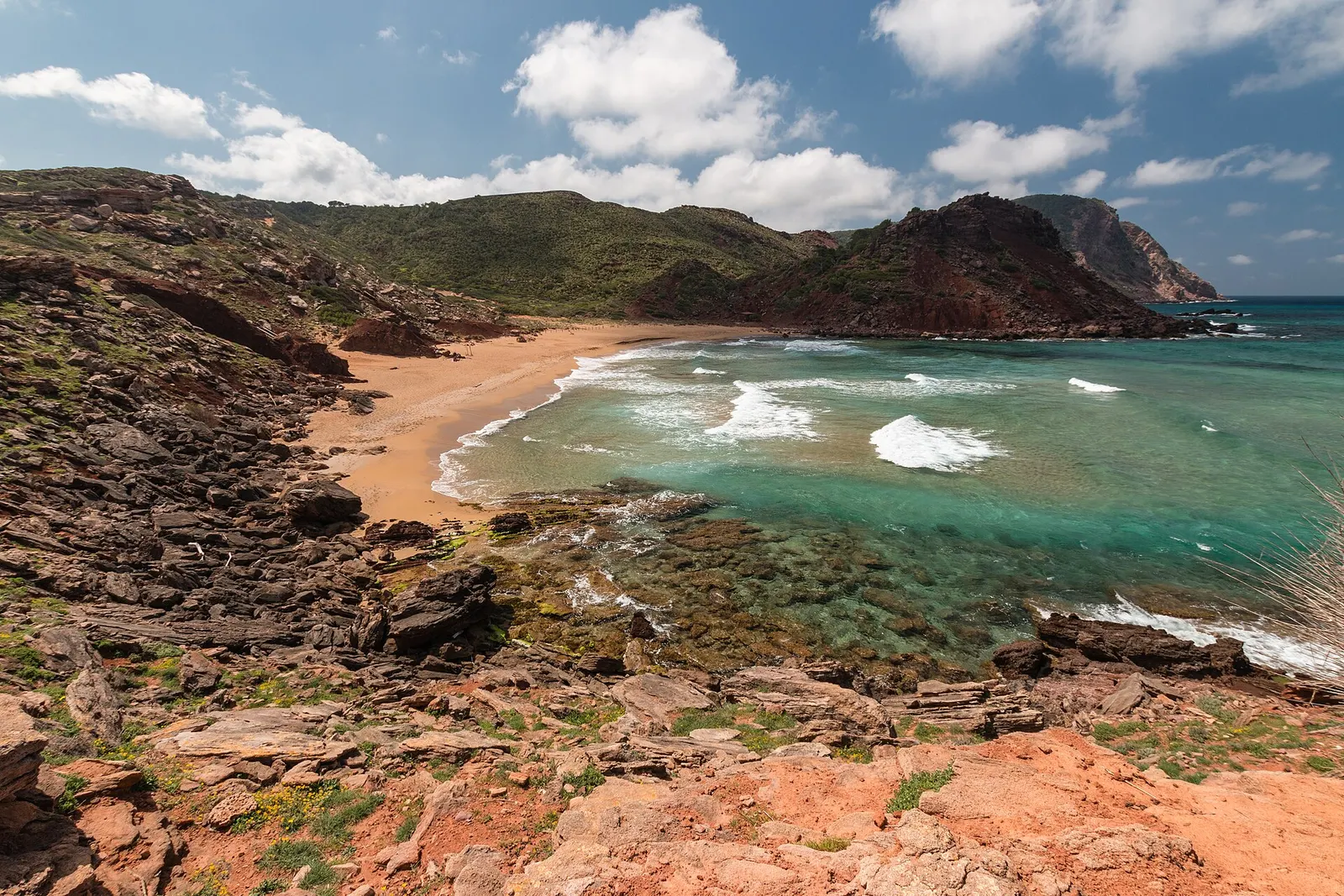 Cala del Pilar vista desde arriba: arena rojiza, agua turquesa y la ladera de monte bajo
