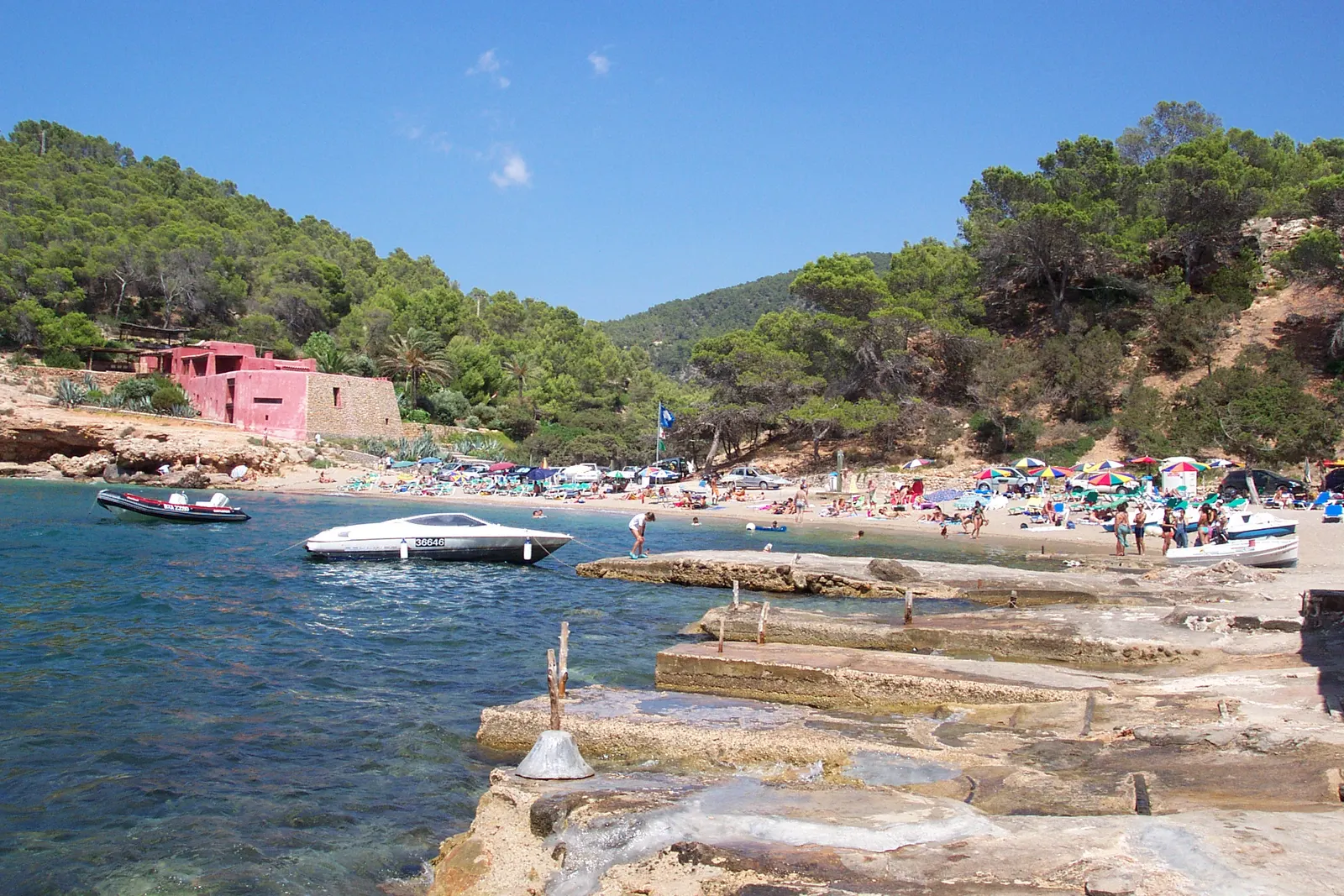 Cala Salada, con las casetas rojas de varadero sobre la roca y el pinar bajando hasta la orilla