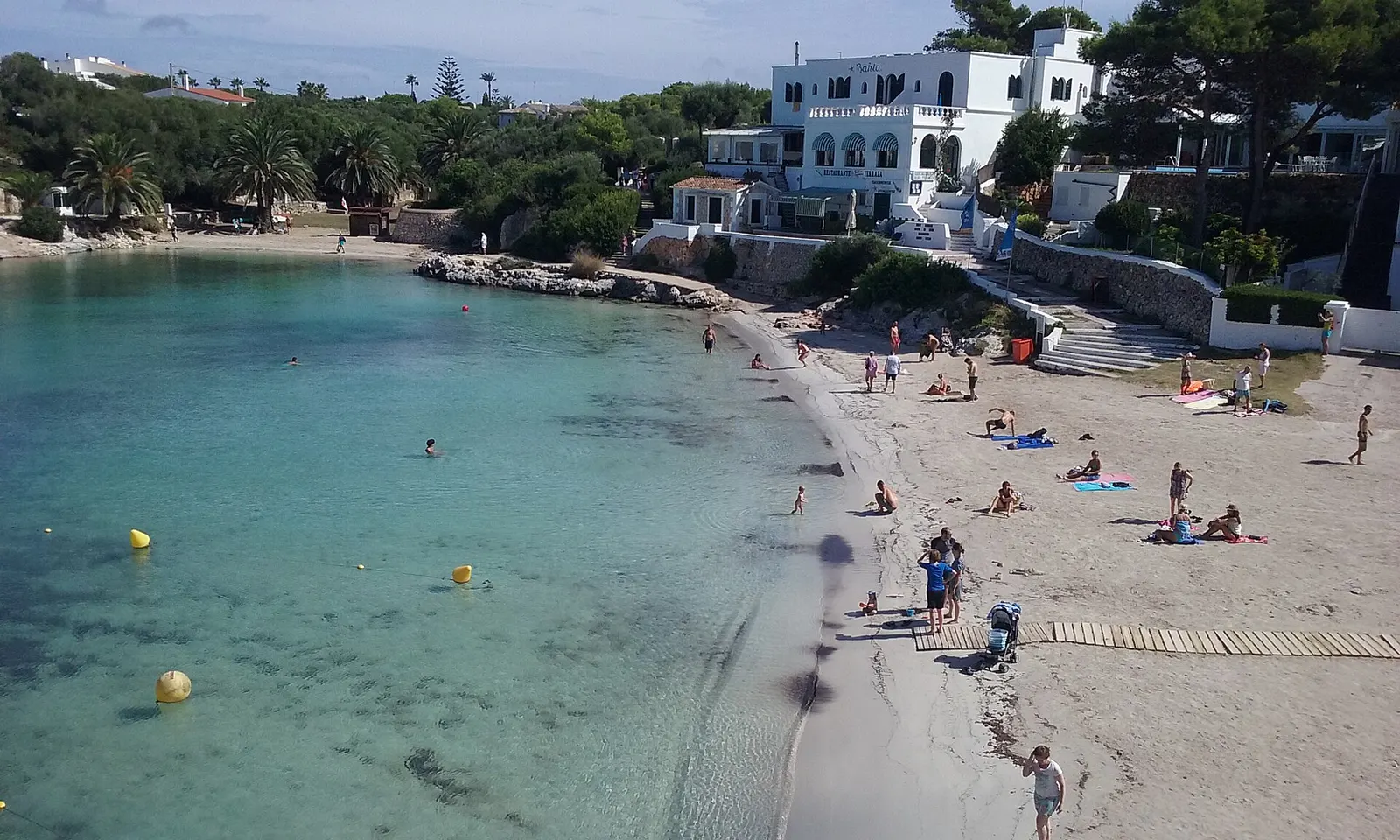 Cala Santandria con la arena, el agua verde clara y las casas blancas sobre la cala