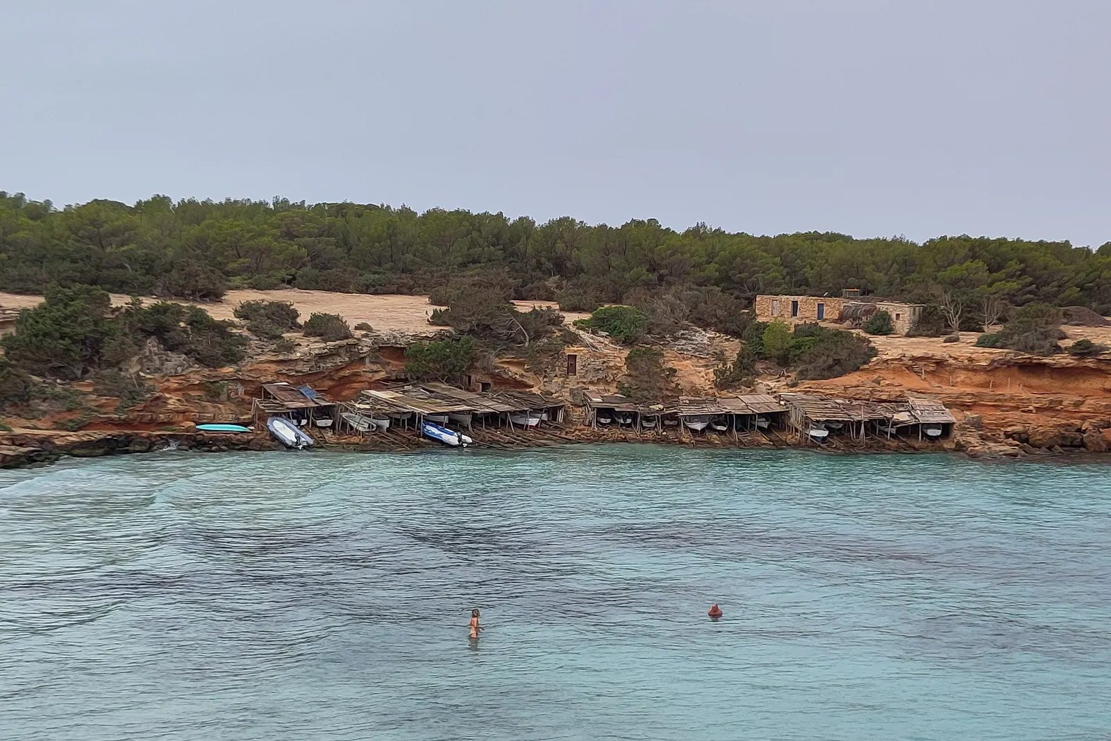 Cala Saona, con las casetas de varadero al borde del agua y el pinar detrás