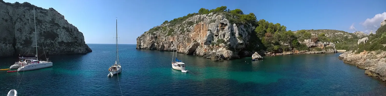 Un velero fondeado en Cales Coves, bajo la pared de roca horadada de cuevas
