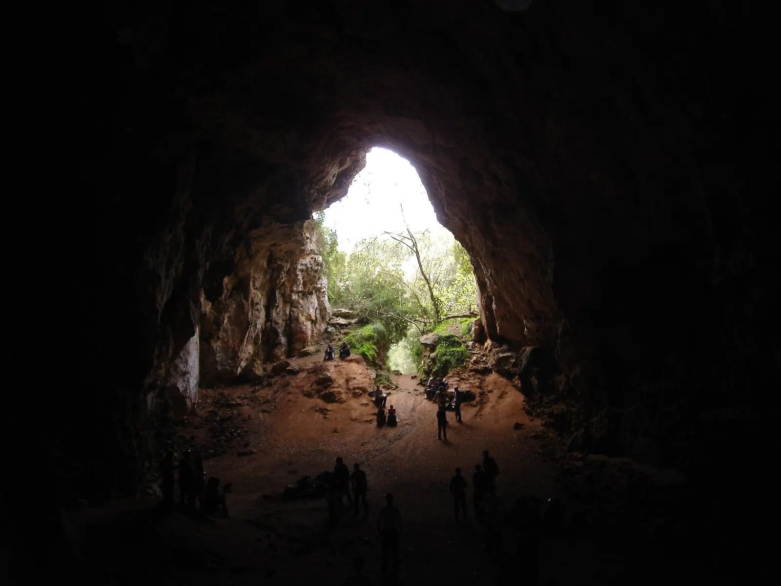 El interior de la Cova des Coloms, con la boca de luz al fondo y personas que dan la escala