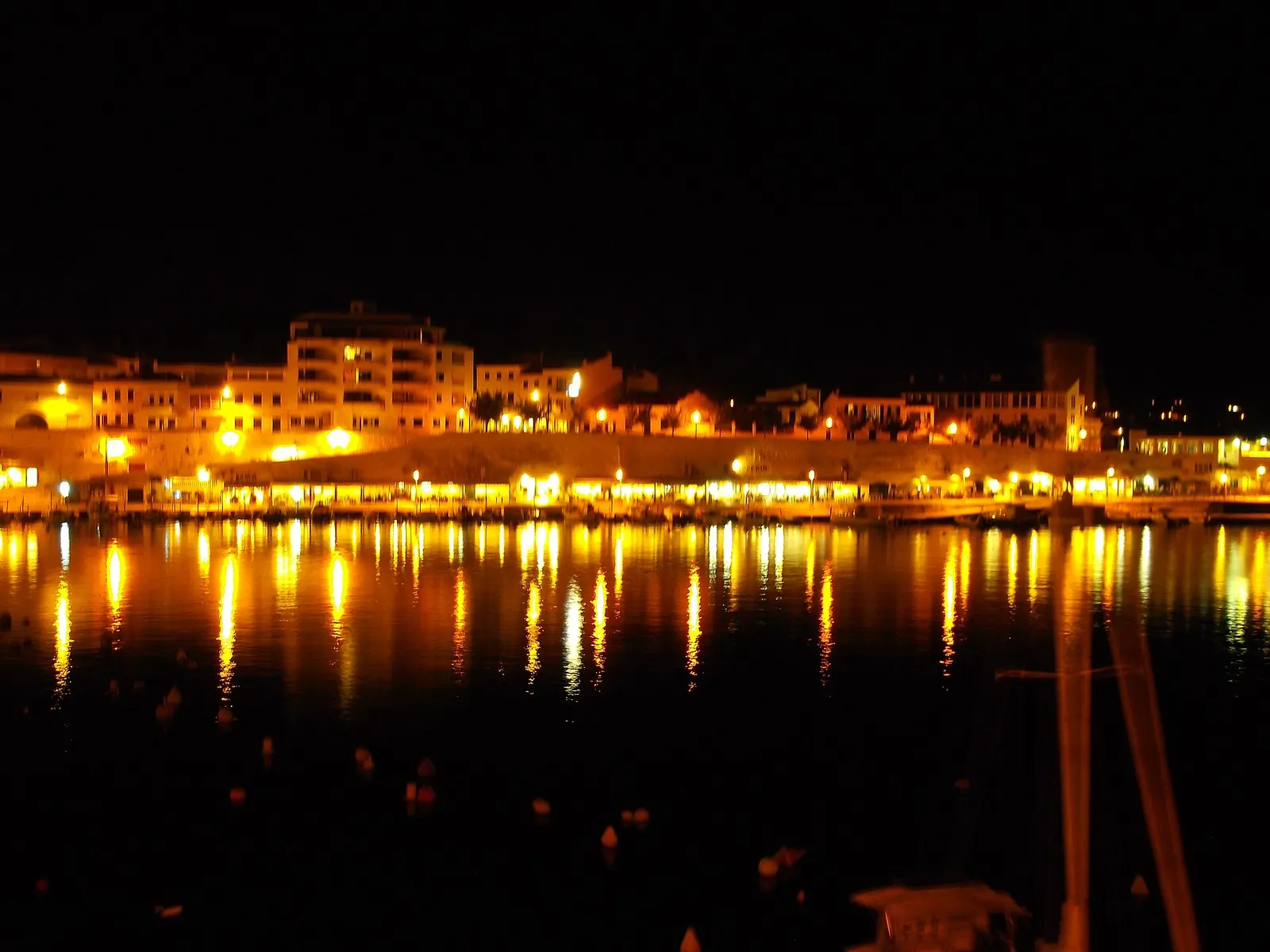 Es Castell de noche, con las luces del muelle reflejadas en el agua