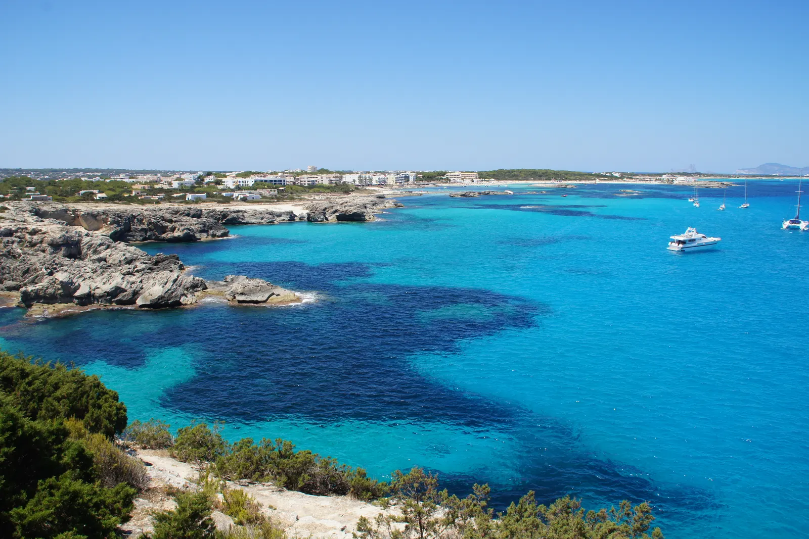 La costa de es Pujols, con el agua turquesa sobre fondo de arena y roca baja