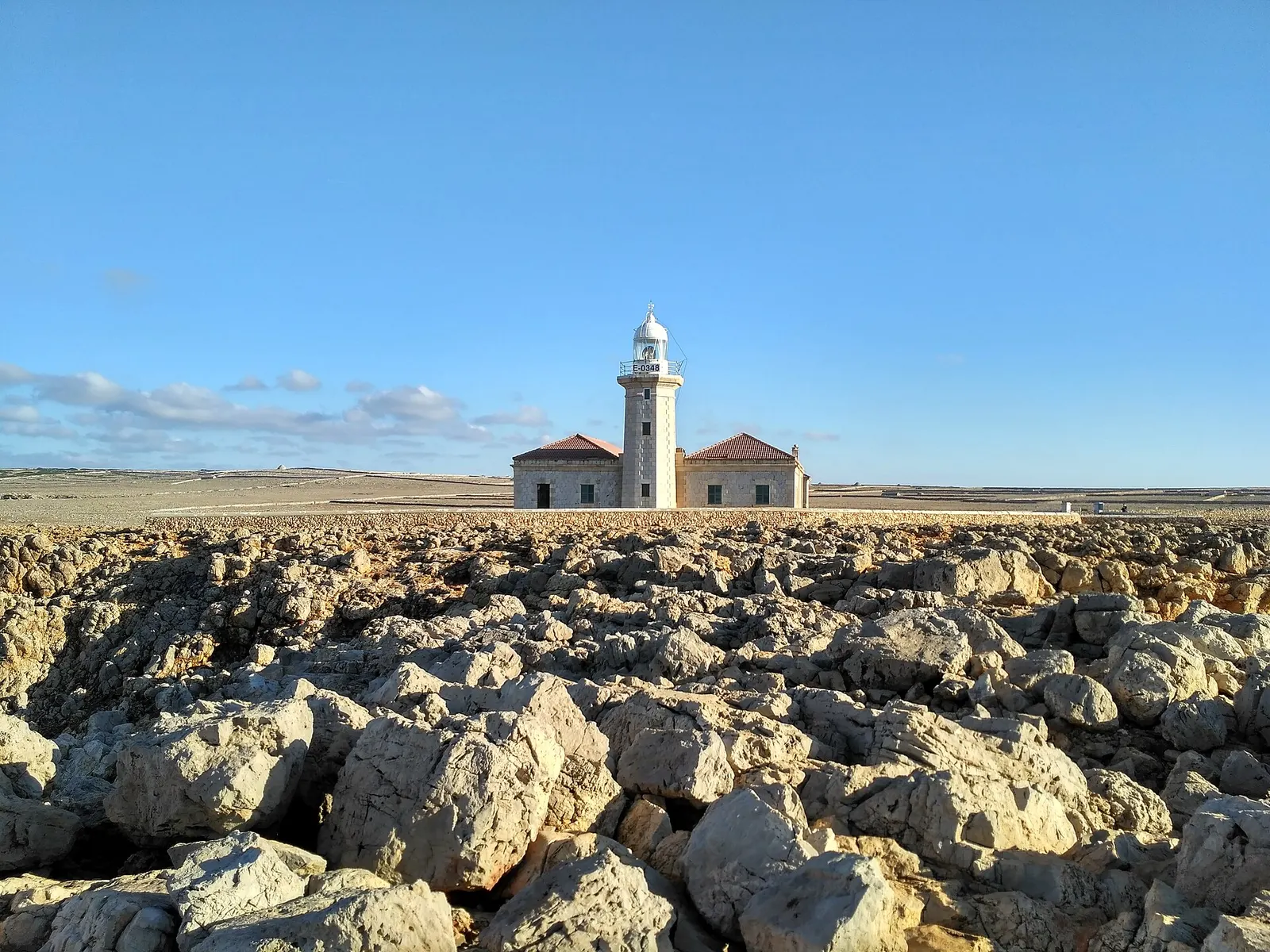 El faro de Punta Nati alzándose sobre un campo de rocas sueltas