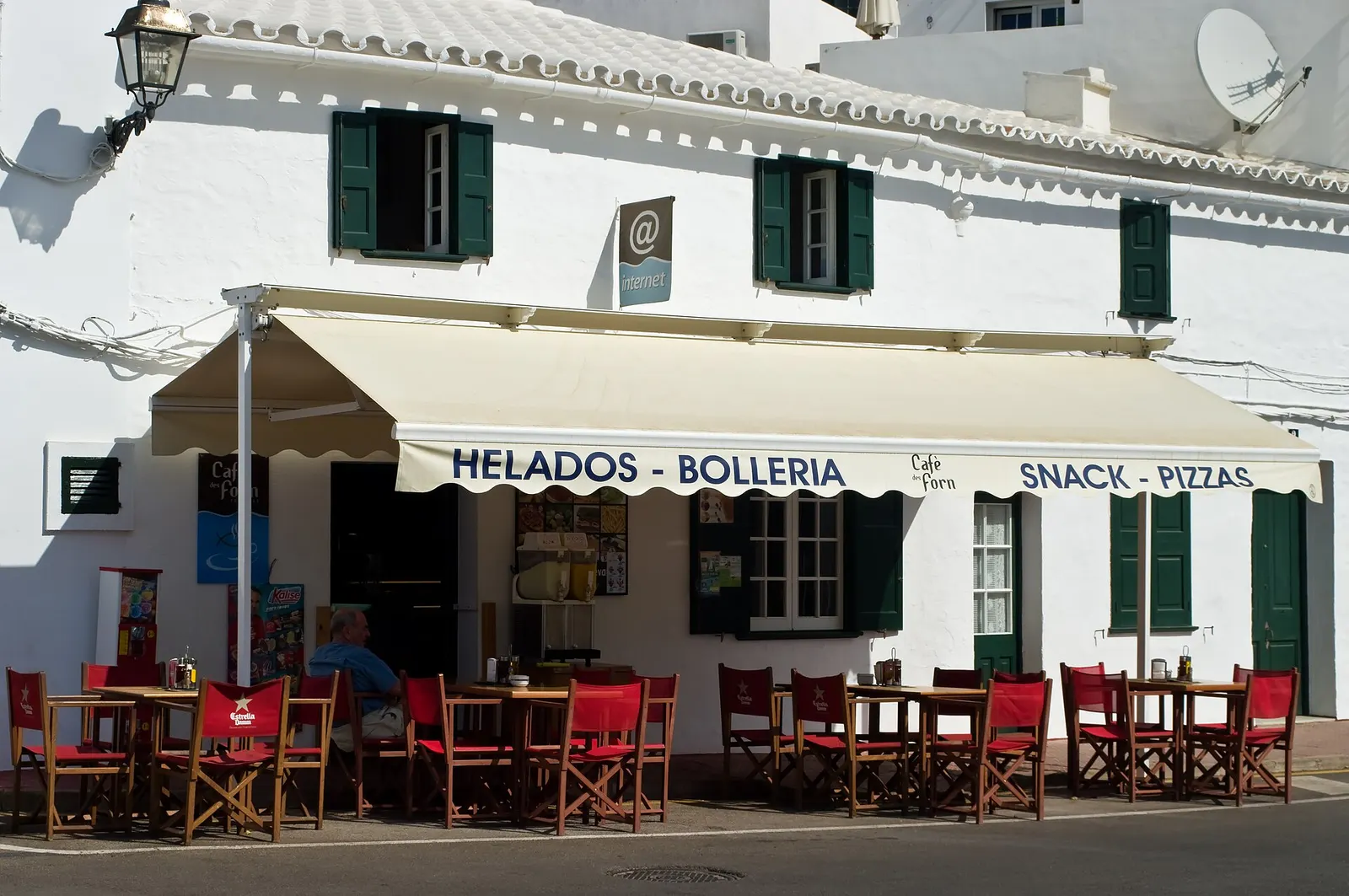 Una fachada blanca de Fornells con el toldo de un café y las persianas verdes