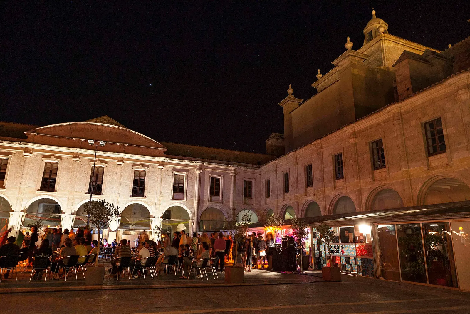 Es Claustre del Carme de Maó de noche, con las arcadas iluminadas y gente en las mesas