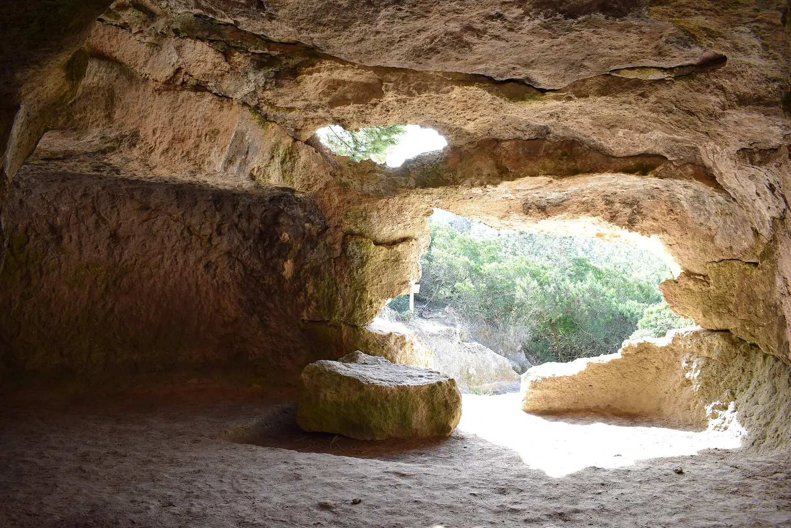 El interior de una cueva funeraria de Cala Morell, excavada en la roca, con la luz entrando por la boca