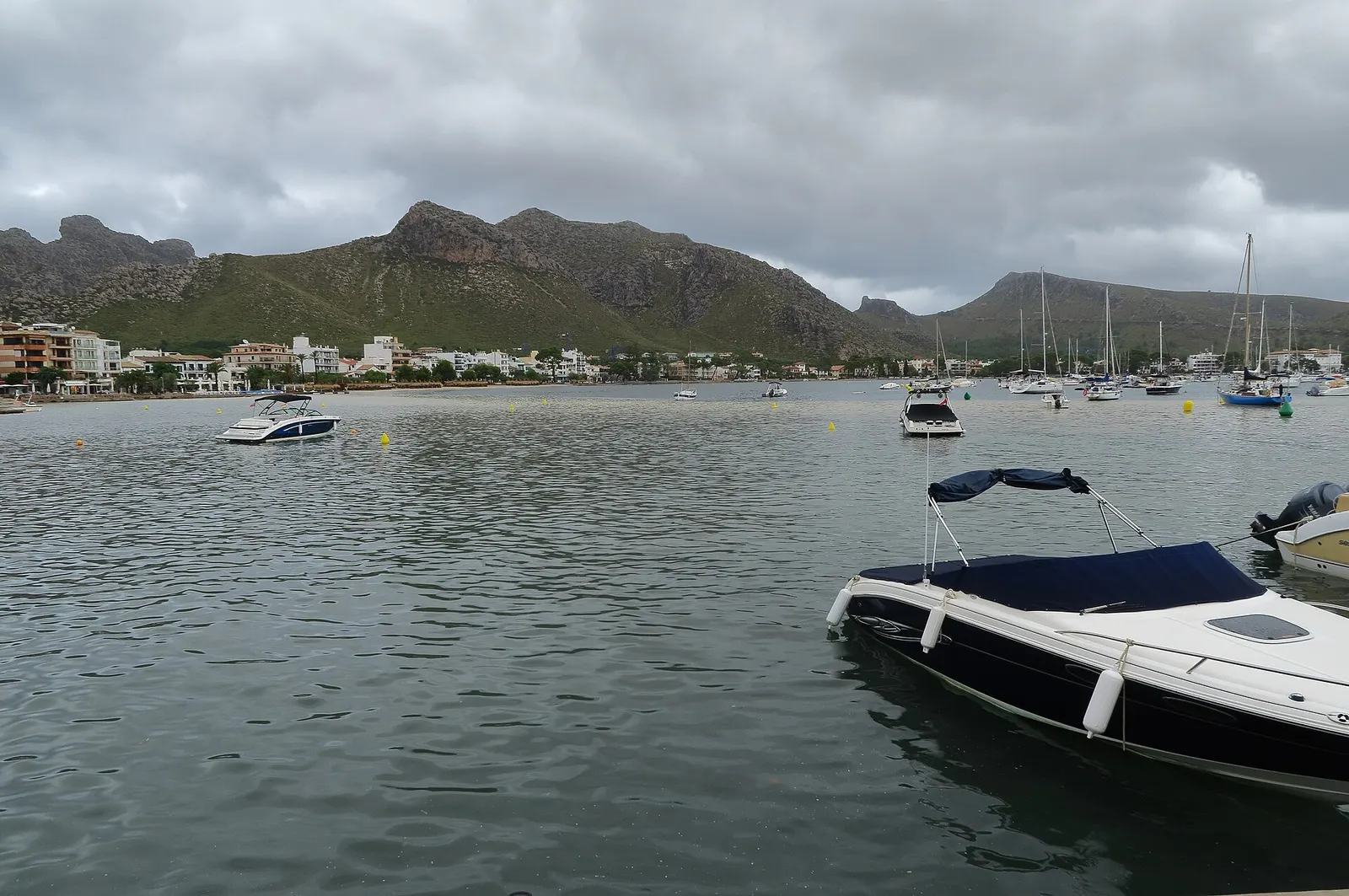 Barcas varadas en la orilla del Port de Pollença, con los veleros fondeados y la montaña detrás