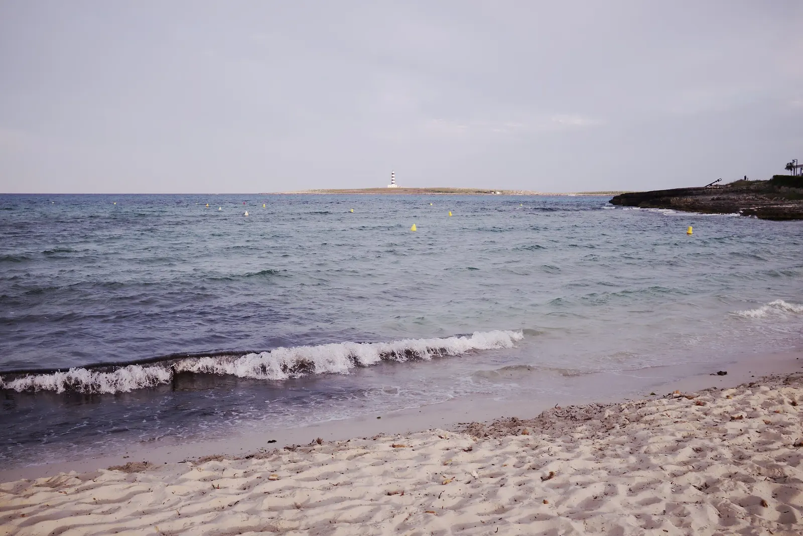 La orilla de Punta Prima, con la Illa de l'Aire y su faro a rayas en el horizonte