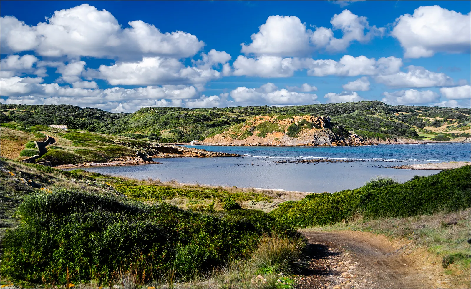 La cala de Sa Torreta desde el camino, entre monte bajo y roca anaranjada
