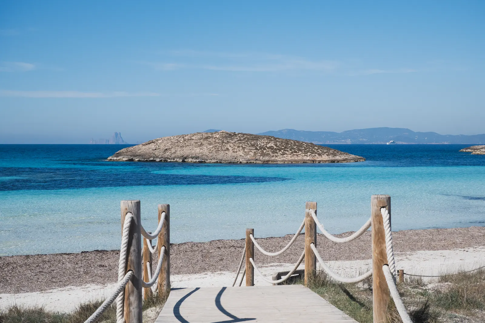 La playa de ses Illetes, con la orilla de arena clara, unos postes de madera y un islote al fondo