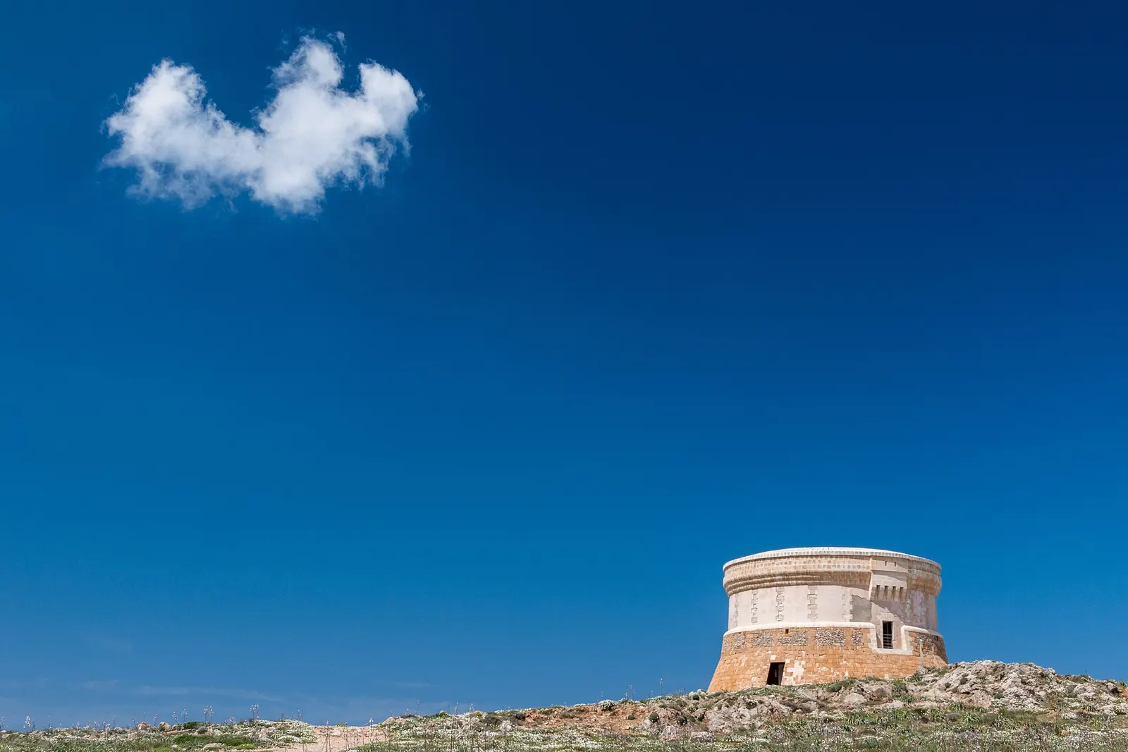 La torre redonda de Fornells recortada sobre el cielo, en lo alto de la loma